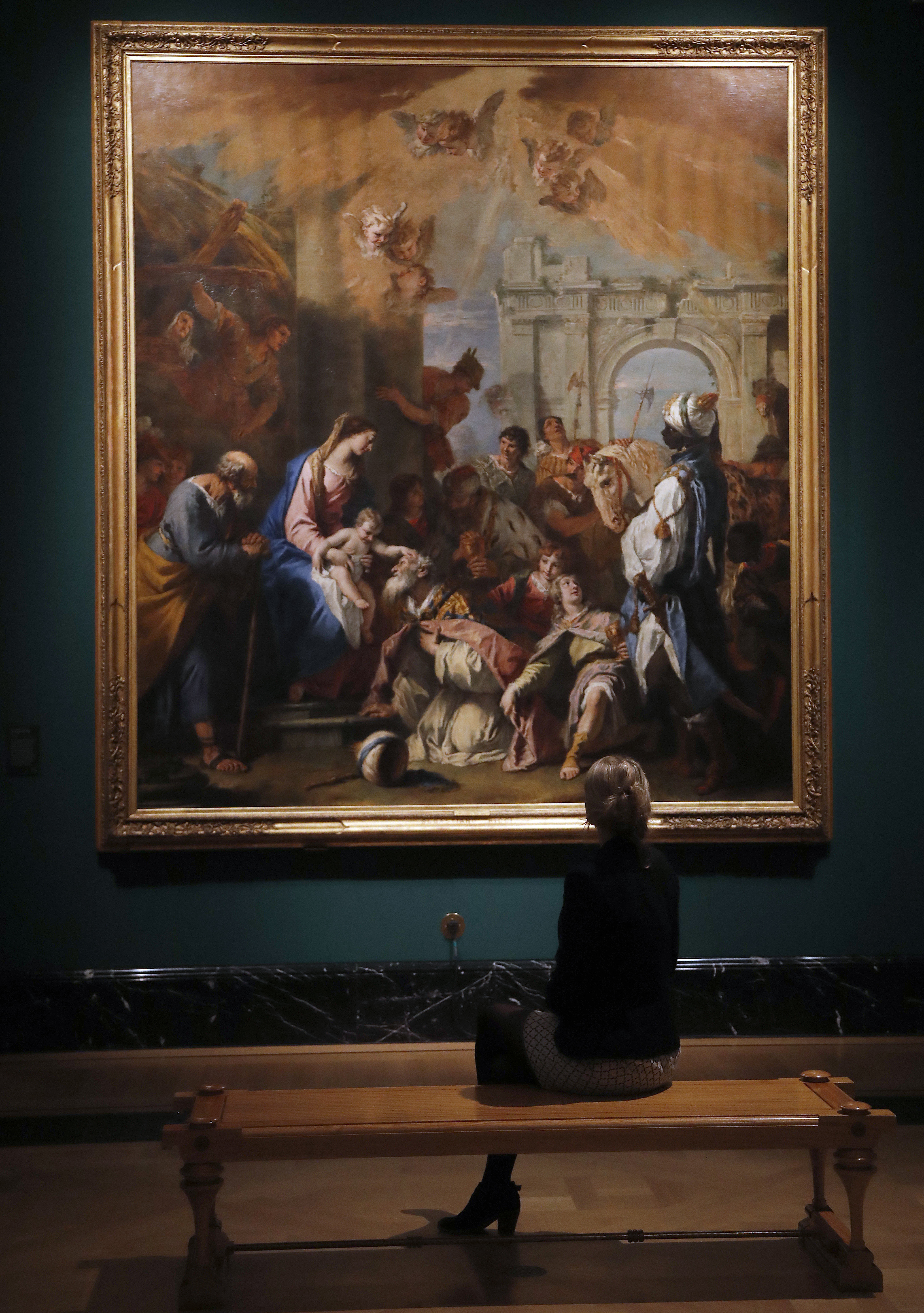 A woman sat down to look at the painting 'The Adoration of the Kings' by Sebastiano Ricci at the Queen's Gallery at Buckingham Palace in London, Thursday, May 18, 2017. A new exhibition reunites two of Canaletto's finest sets of paintings, displayed side by side for the first time in almost 40 years. Canaletto & the Art of Venice is opening on May 19, at The Queen's Gallery, Buckingham Palace. (AP Photo/Frank Augstein)