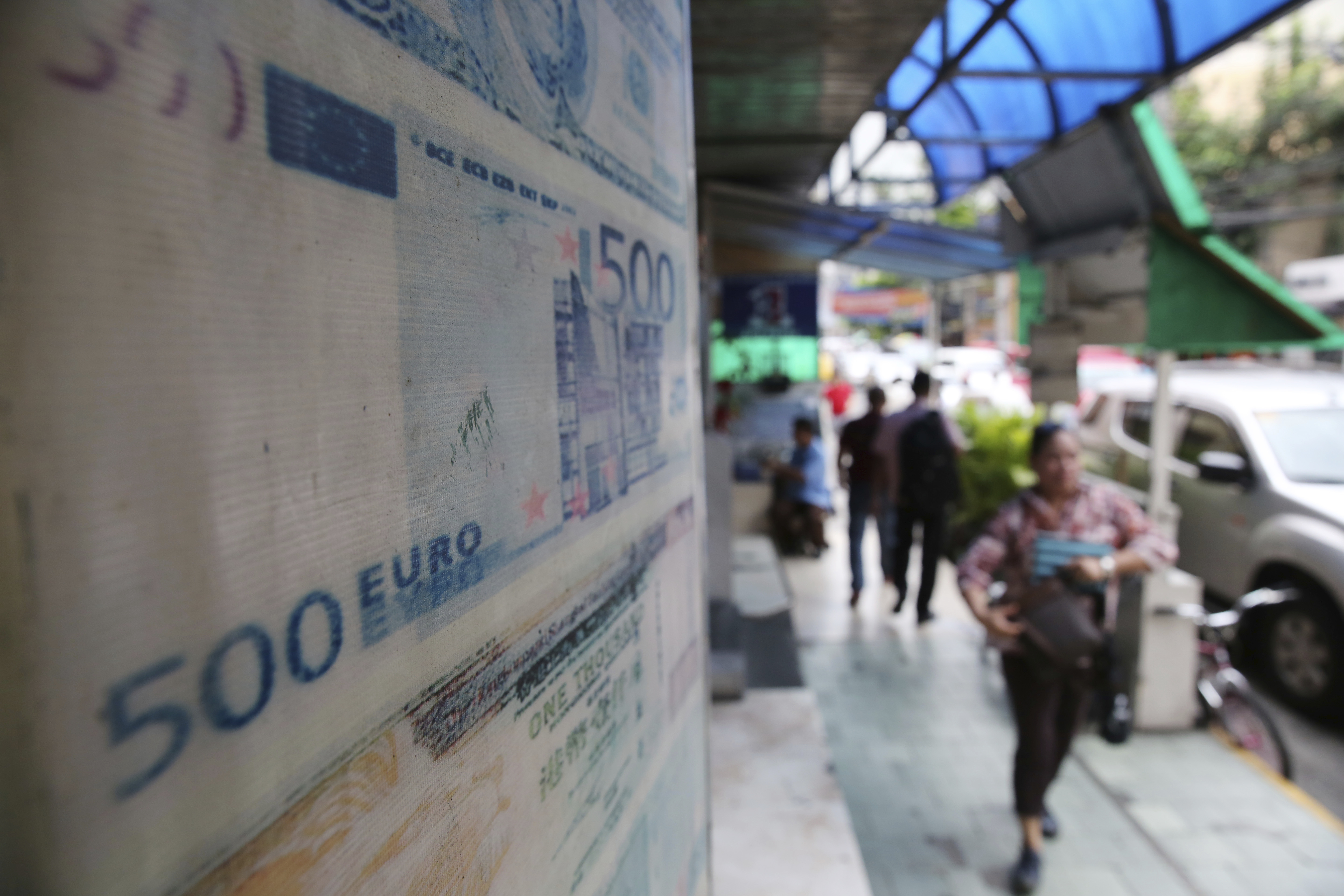 People pass by a 500 Euro bill that is posted on a tarpaulin outside a money changer in Manila, Philippines Thursday, May 18, 2017. The Philippines will no longer accept assistance from the European Union, forgoing grants possibly worth more than 250 million euros ($ 278.7 million) for development projects in the country following President Rodrigo Duterte's earlier challenge on the EU to stop its assistance after the bloc warned that the Philippines risks losing tariff-free exports to Europe because of the thousands killed in the war on drugs launched by Duterte and Manila's moves to revive the death penalty. The EU delegation in Manila said the Philippine government informed it about its decision Wednesday, but it has yet to receive a written notice. (AP Photo/Aaron Favila)