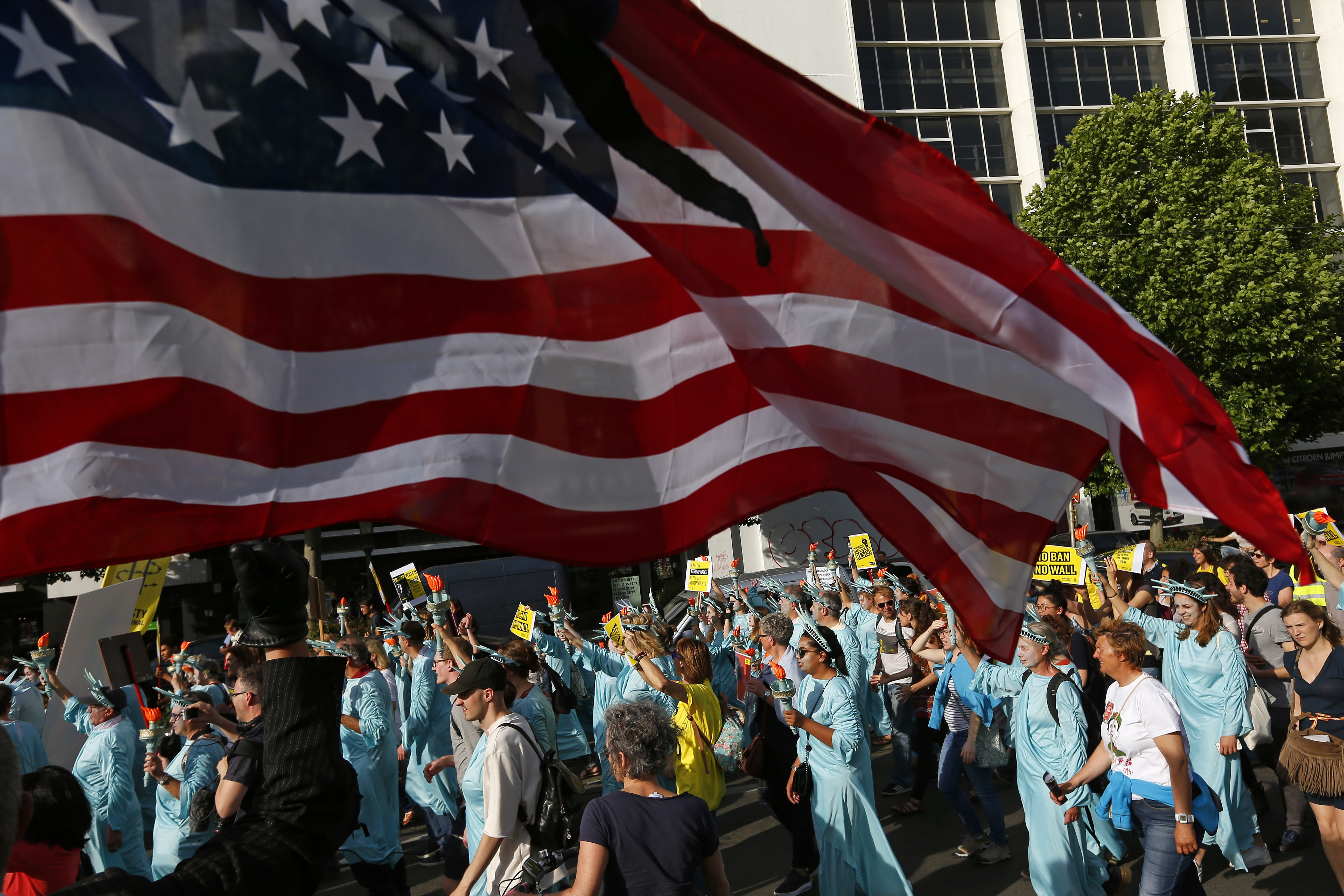 Protesters dressed as the Statue of Liberty march under a US flag during a demonstration in the center of Brussels on Wednesday, May 24, 2017. Demonstrators marched in Brussels ahead of a visit of US President Donald Trump and a NATO heads of state summit which will take place on Thursday. (AP Photo/Peter Dejong)
