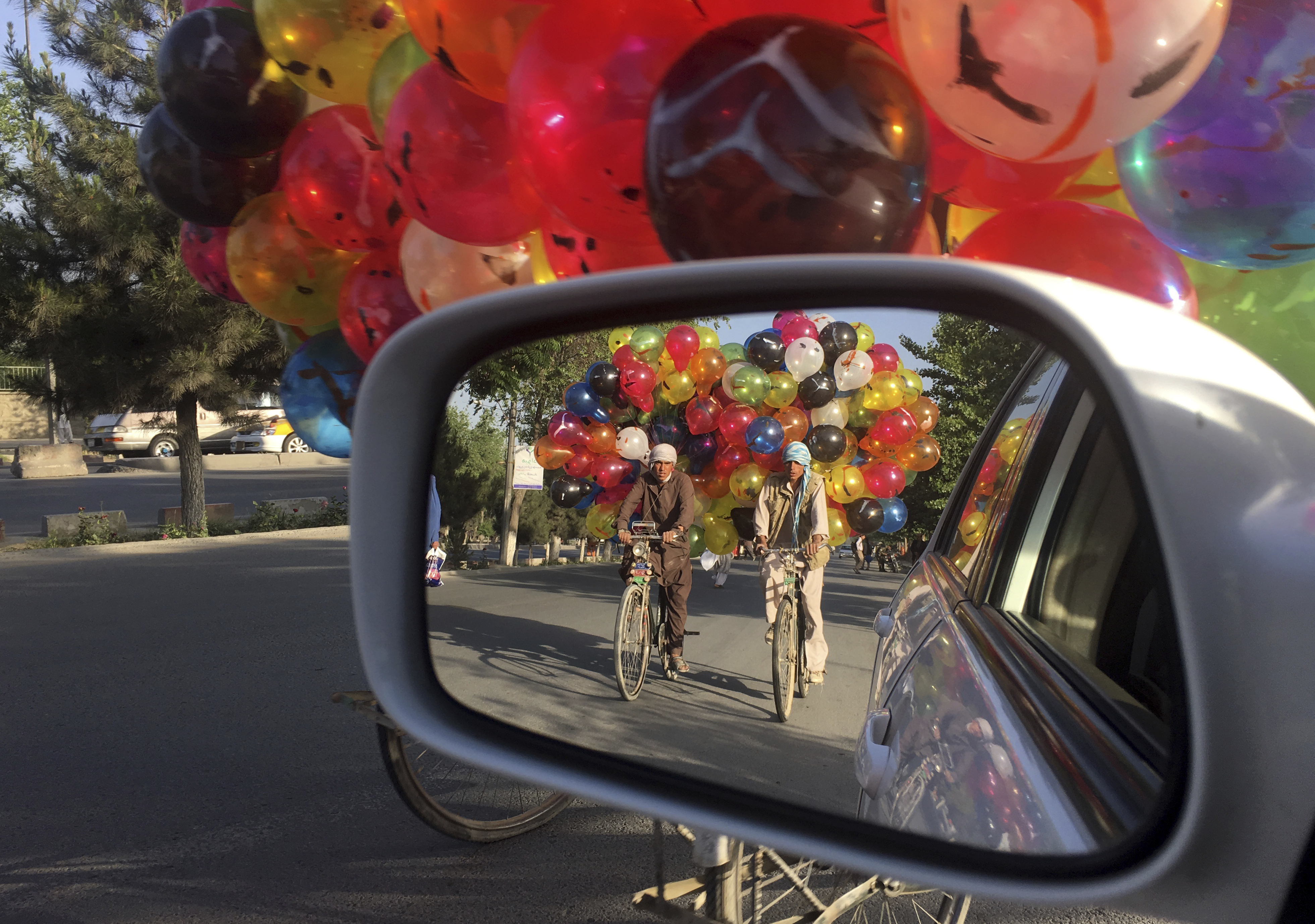 Afghan balloon vendors riding their bicycles, are reflected in the mirror of a car in Kabul, Afghanistan, Sunday, May 21, 2017. (AP Photo/Rahmat Gul)