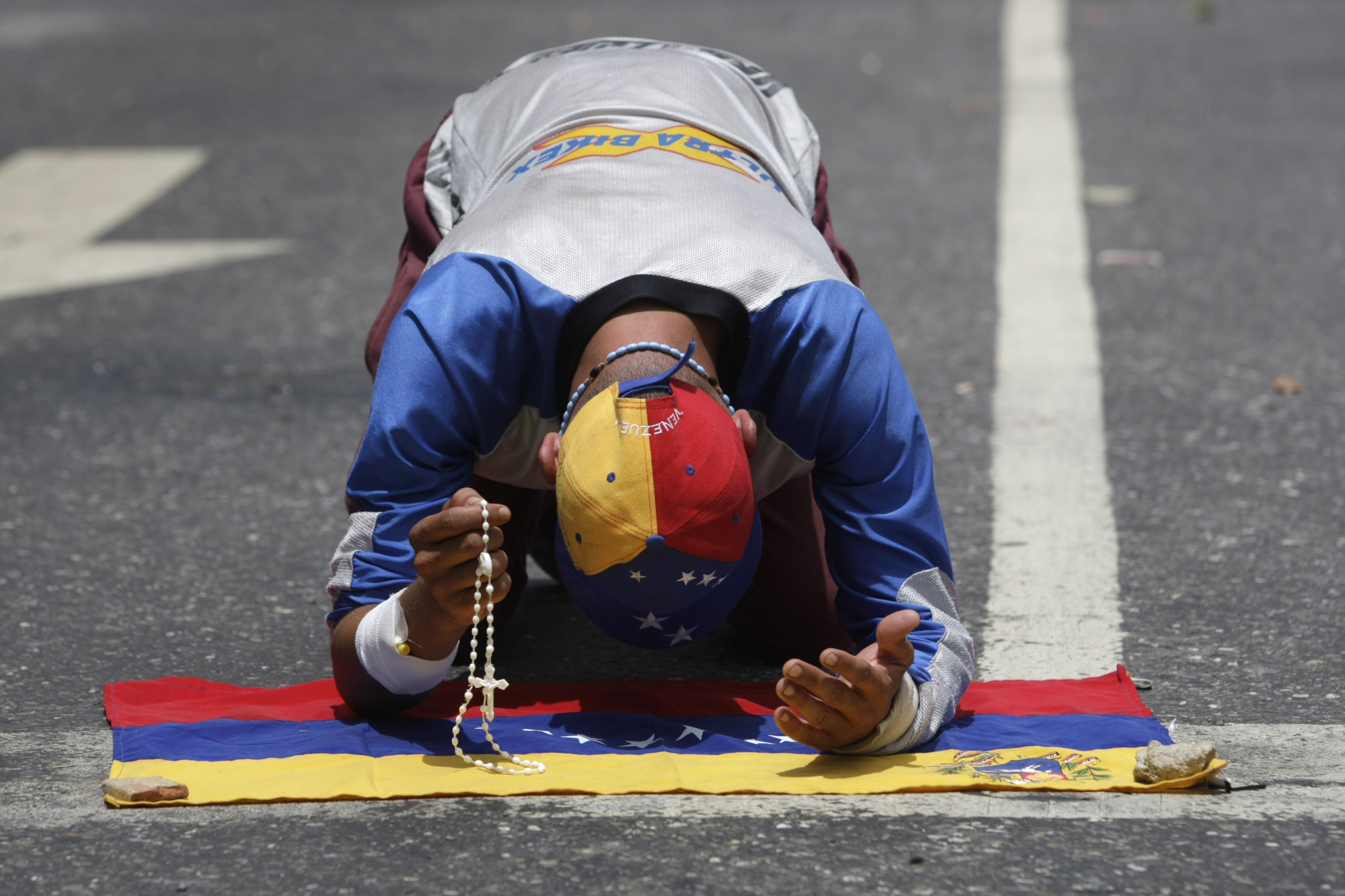 A demonstrator holding a rosary prays over a Venezuelan flag prior to a march against the government of President Nicolas Maduro in Caracas, Venezuela, Wednesday, May 31, 2017. Protests have left dozens dead in the last two months as the opposition demands immediate presidential elections and the liberation of political prisoners. (AP Photo/Fernando Llano)