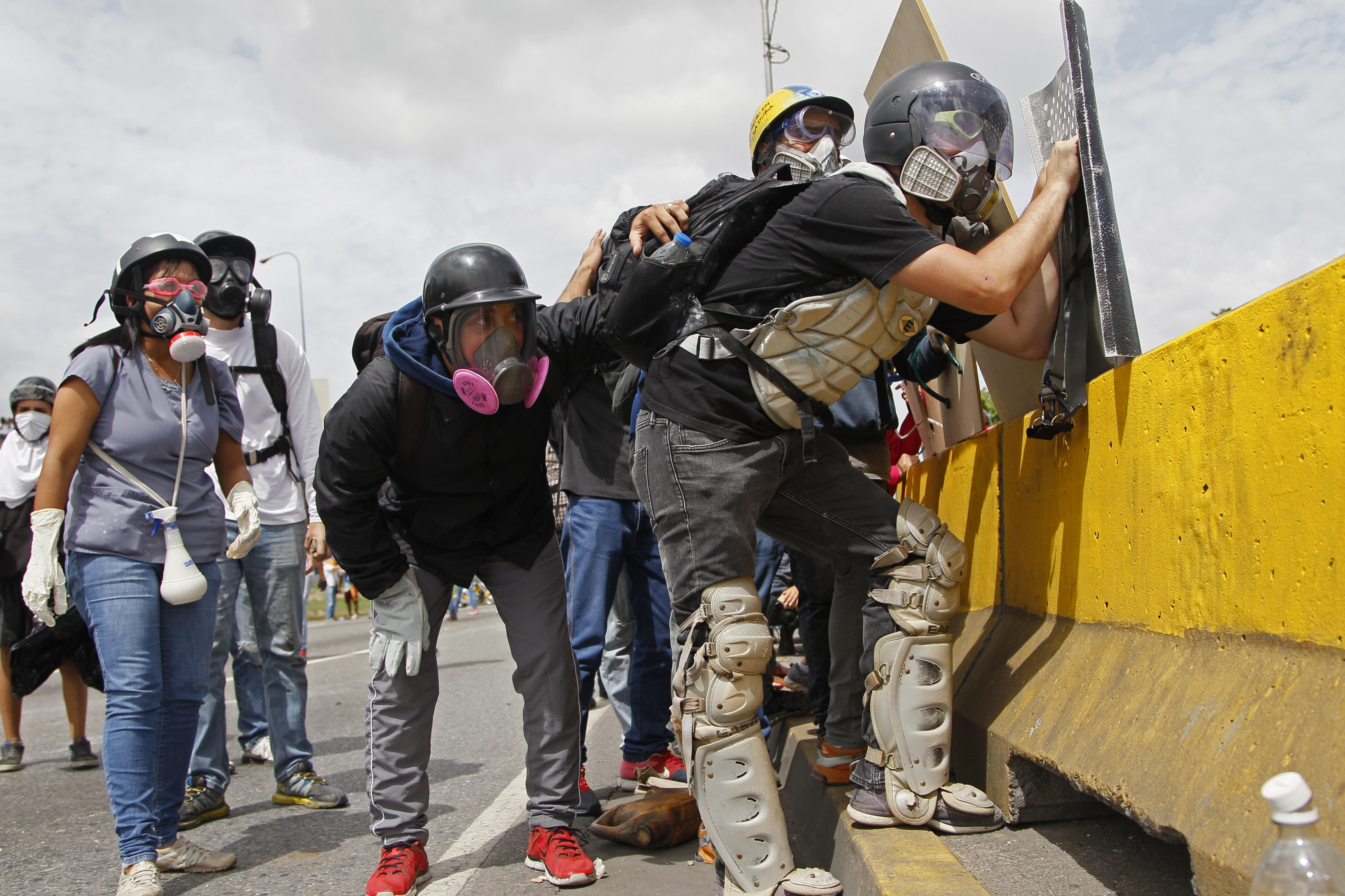A demonstrator wearing baseball catchers' gear takes cover behind a highway median during clashes with government forces at a march against the government of President Nicolas Maduro in Caracas, Venezuela, Wednesday, May 31, 2017. Protests have left dozens dead in the last two months. The opposition wants immediate presidential elections and the liberation of political prisoners. (AP Photo/Ariana Cubillos)
