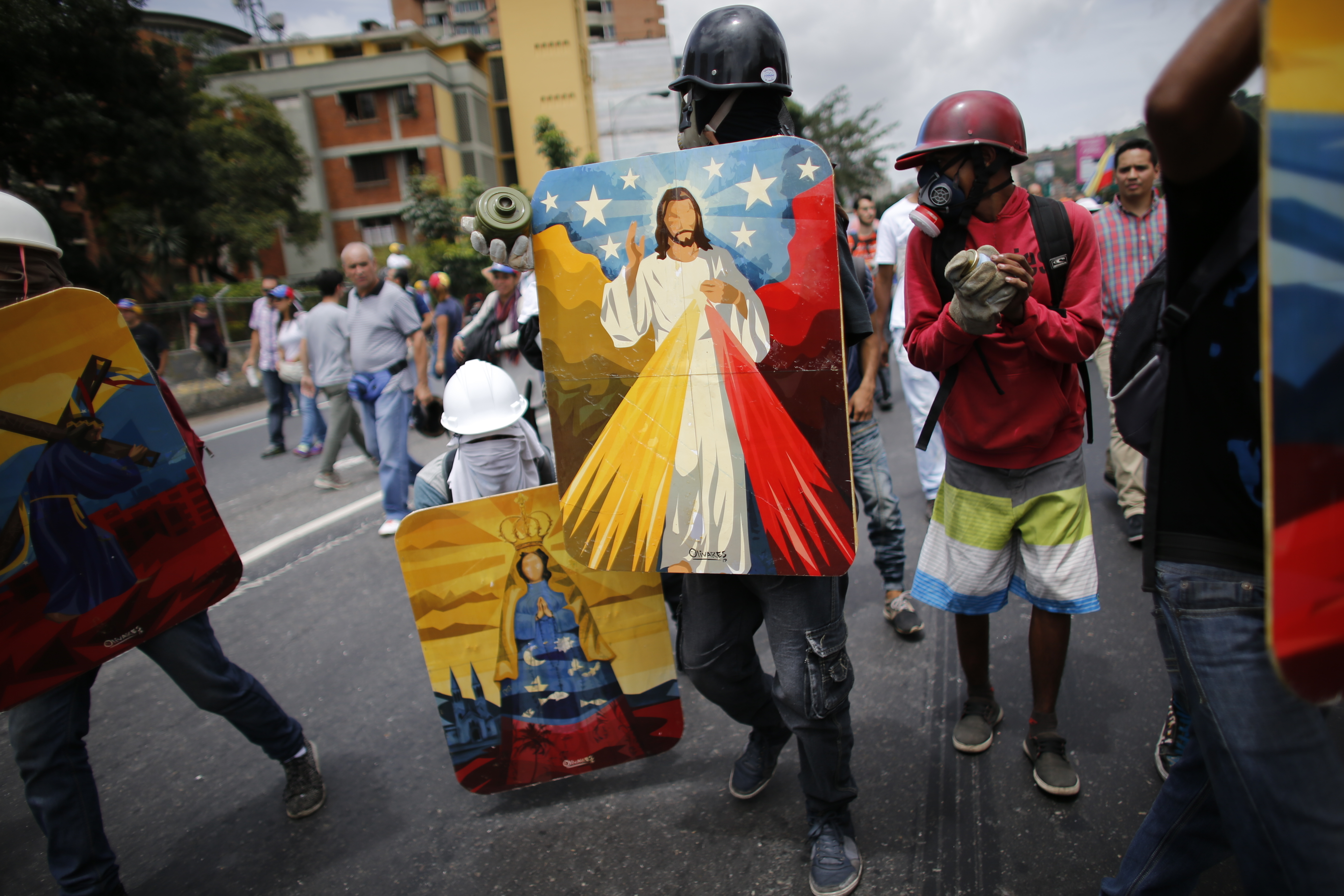 Demonstrators use shields decorated with religious motifs and the colors of Venezuela's national flag prior clashing with government forces on a highway during a march against the government of President Nicolas Maduro in Caracas, Venezuela, Wednesday, May 31, 2017. Protests have left dozens dead in the last two months as the opposition demands immediate presidential elections and the liberation of political prisoners. (AP Photo/Ariana Cubillos)