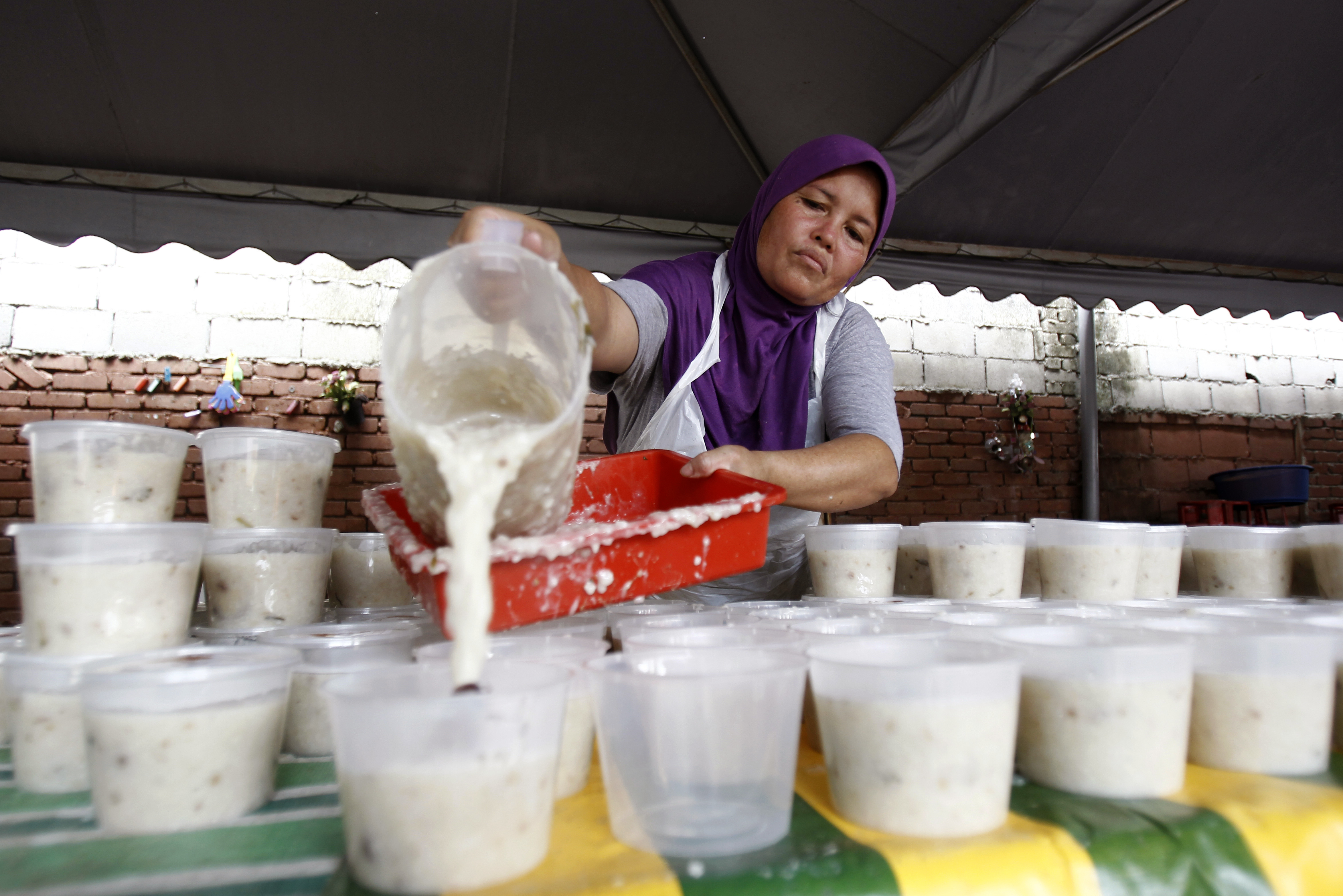 A woman pours Bubur Lambuk porridge into containers at the Kampung Baru village in Kuala Lumpur, Malaysia on Thursday, June 1, 2017. Bubur Lambuk is a type of Malay rice porridge that is cooked and distributed in many places during the fasting month of Ramadan. (AP Photo/Daniel Chan)