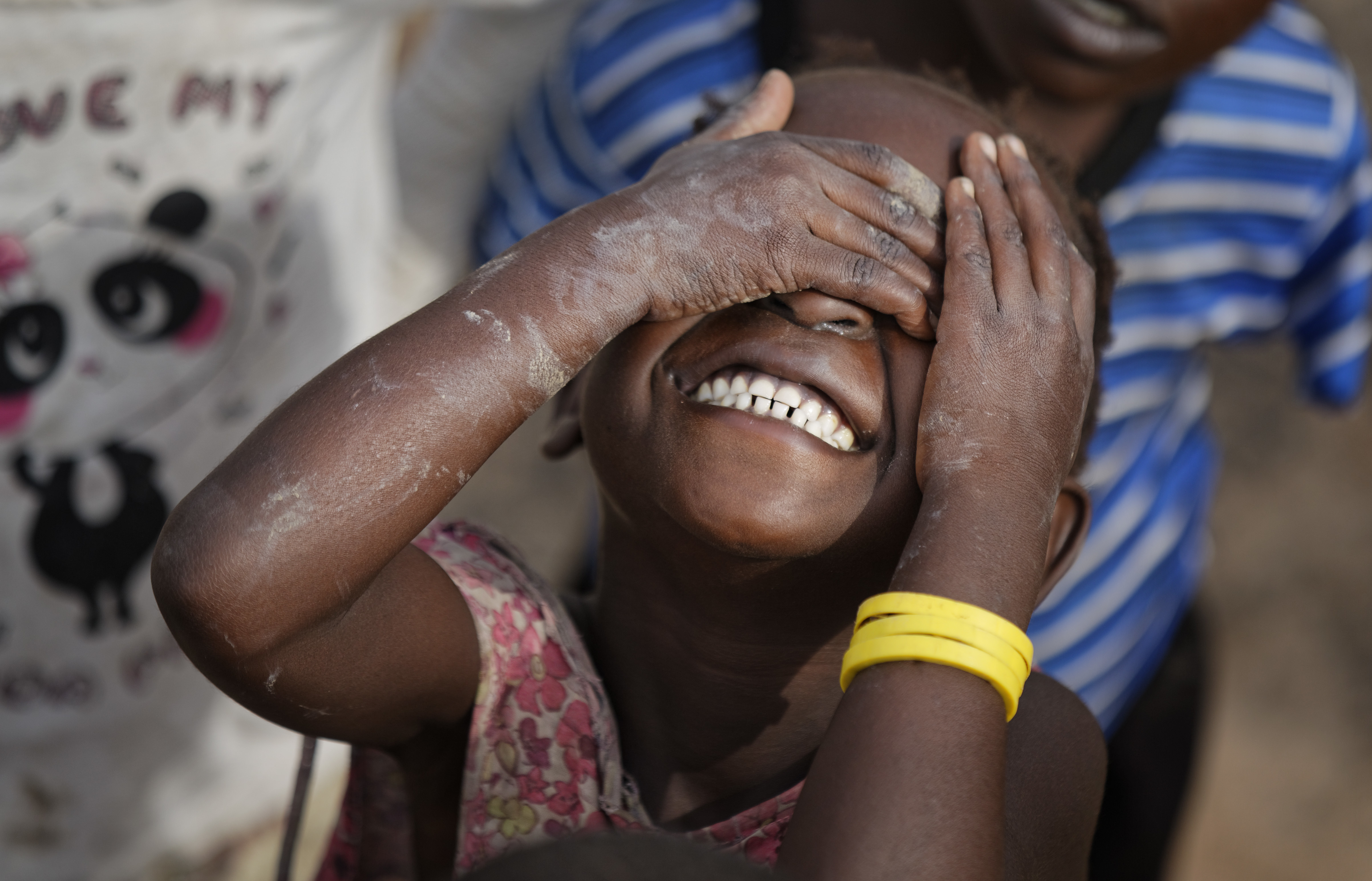 A young South Sudanese refugee girl laughs and hides her face from the camera during morning break in the yard of the Ombechi nursery school, which has over 500 pupils and is supported by UNICEF and Save the Children, in Bidi Bidi, Uganda Wednesday, June 7, 2017. Bidi Bidi is a sprawling complex of mud-brick houses that is now the world's largest refugee settlement holding some of those who fled the civil war in South Sudan, which has killed tens of thousands and driven out more than 1.5 million people in the past three years, creating the world's largest refugee crisis. (AP Photo/Ben Curtis)