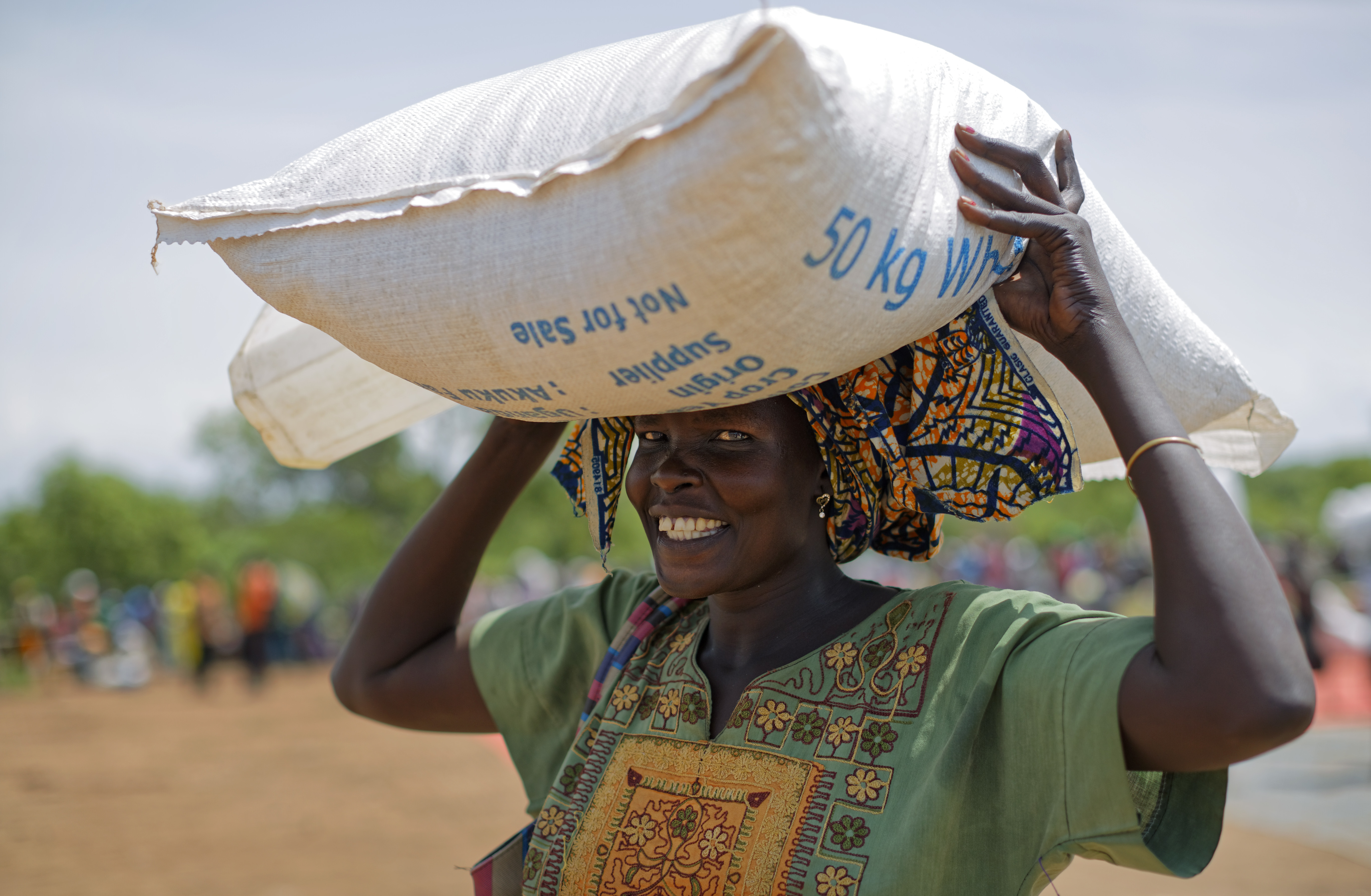 A South Sudanese refugee woman smiles as she carries away a heavy sack of maize after receiving a food distribution in Bidi Bidi, Uganda Wednesday, June 7, 2017. Bidi Bidi is a sprawling complex of mud-brick houses that is now the world's largest refugee settlement holding some of those who fled the civil war in South Sudan, which has killed tens of thousands and driven out more than 1.5 million people in the past three years, creating the world's largest refugee crisis. (AP Photo/Ben Curtis)