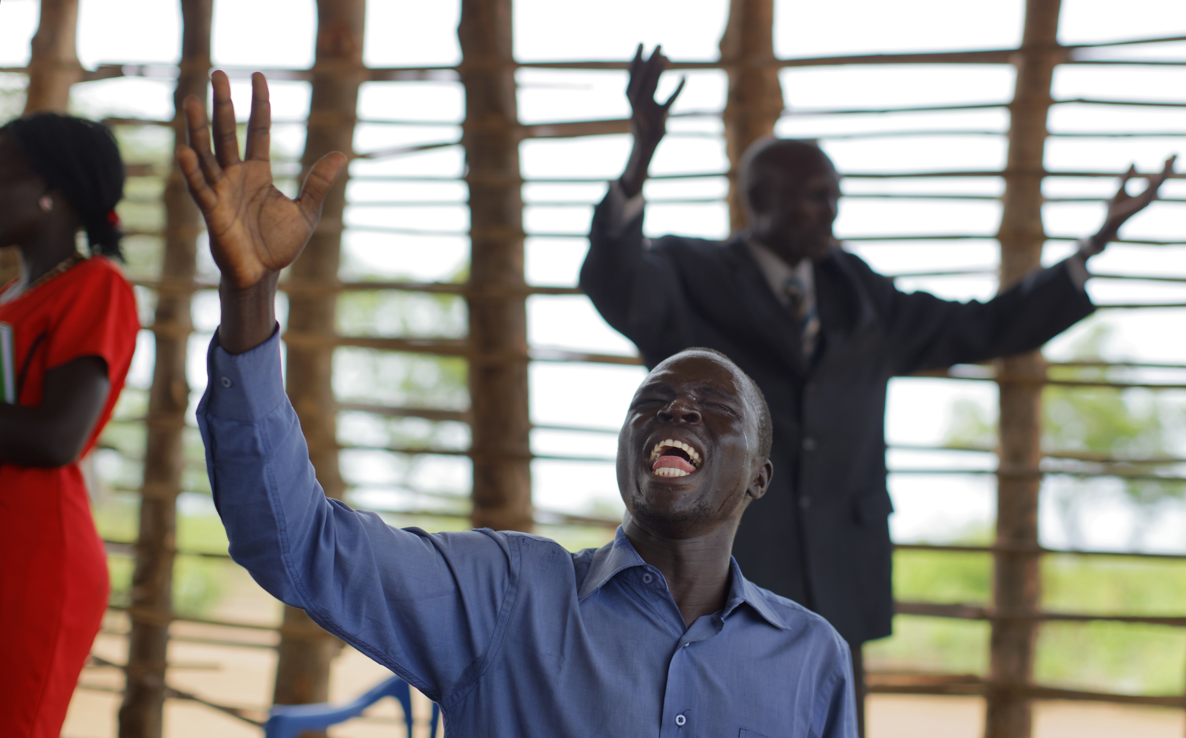In this photo taken Sunday, June 4, 2017, preacher Daniel Rasash falls to his knees and weeps in prayer, at the Yoyo Pentecostal Church in Bidi Bidi refugee settlement in northern Uganda. The South Sudanese refugees meet in open-air churches rigged from timber with seats made only from planks of wood or logs drilled into the ground, yet these churches for the born-again Christians are oases of joy among the daily humiliations that come with rebuilding their lives. (AP Photo/Ben Curtis)