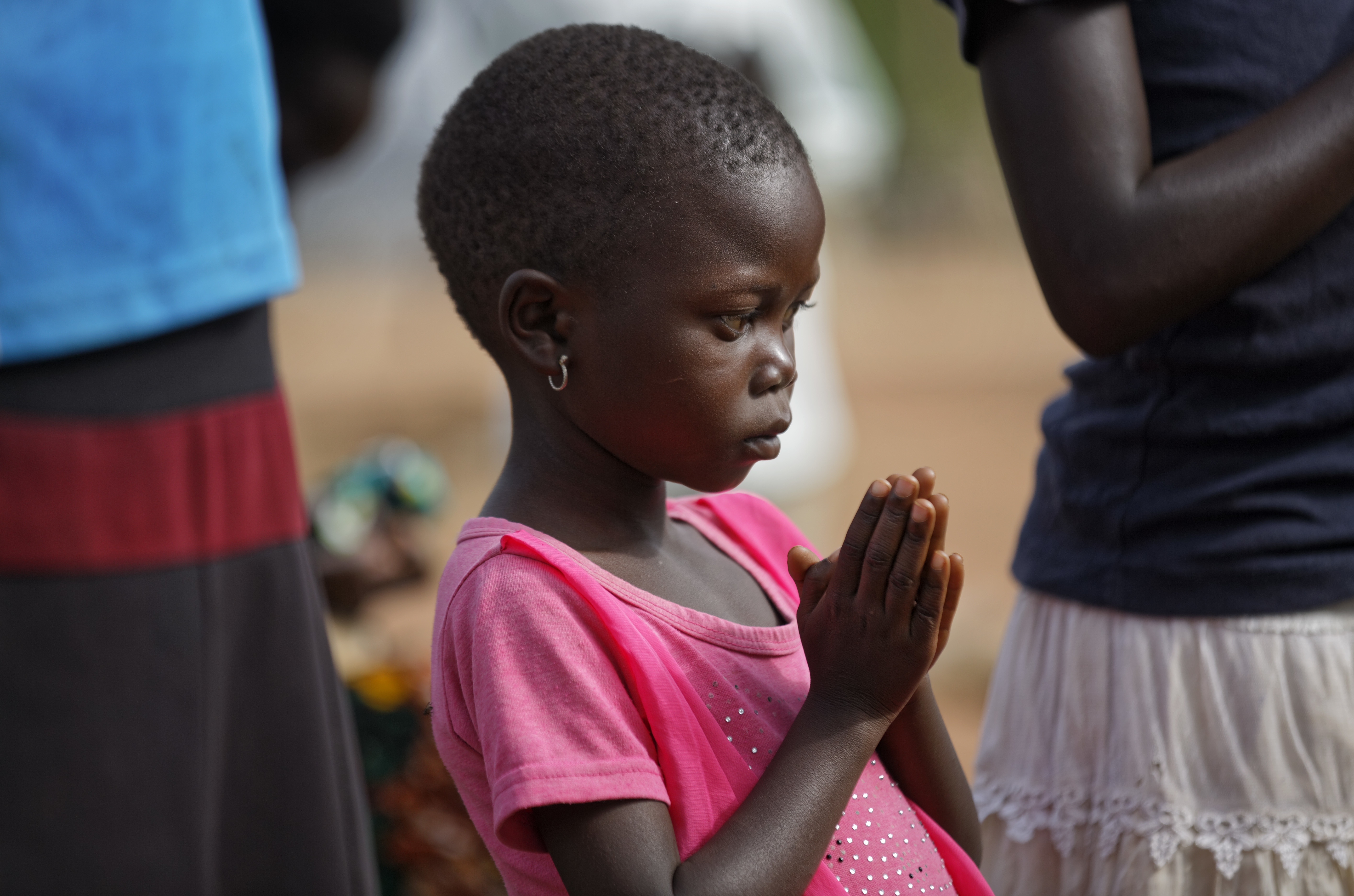 In this photo taken Sunday, June 4, 2017, a young member of the congregation prays at a pentecostal born-again church in Bidi Bidi refugee settlement in northern Uganda. The South Sudanese refugees meet in open-air churches rigged from timber with seats made only from planks of wood or logs drilled into the ground, yet these churches for the born-again Christians are oases of joy among the daily humiliations that come with rebuilding their lives. (AP Photo/Ben Curtis)