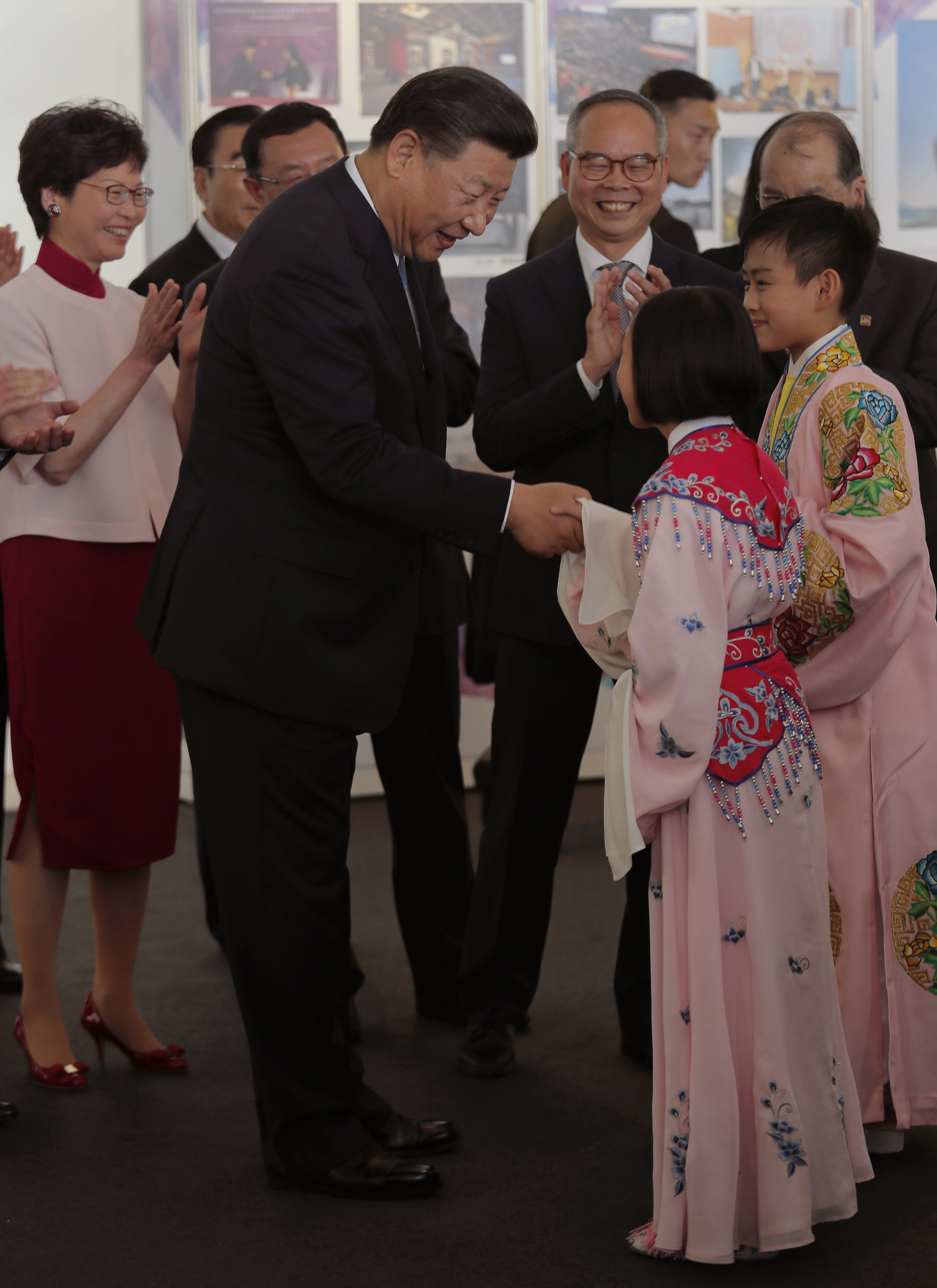 Chinese President Xi Jinping, center, shakes hands with two young Chinese opera performers as Hong Kong Chief Executive-elect Carrie Lam, left, applauds during a visit to Hong Kong's West Kowloon district Thursday, June 29, 2017, the site of a controversial high speed cross-border rail terminus. Pro-democracy supporters fear that a plan to station mainland Chinese immigration agents in the terminal to check passengers departing on trains for the mainland is an erosion of Hong Kong's 