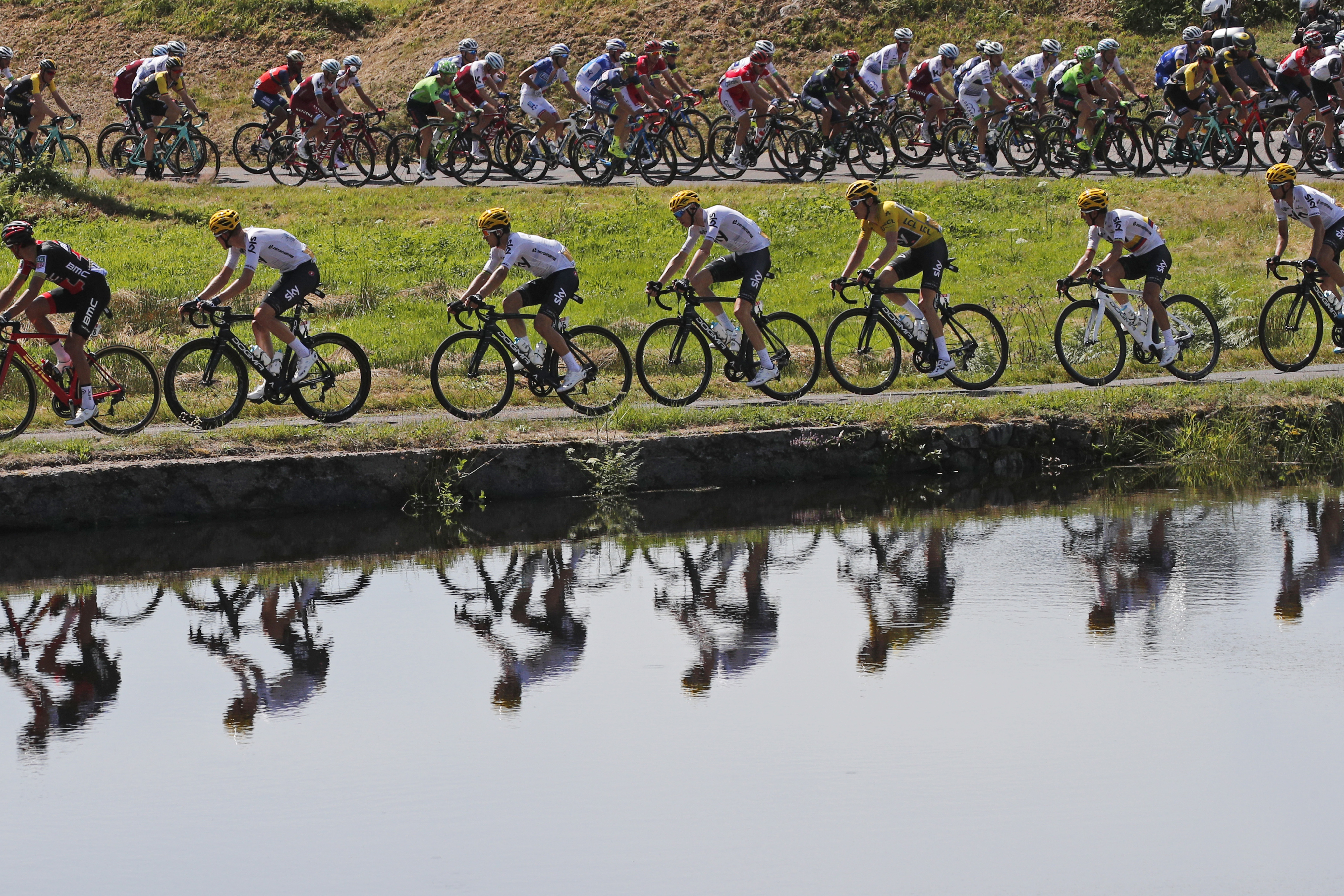 The pack with Britain's Geraint Thomas, wearing the overall leader's yellow jersey, is reflected in a pond during the fifth stage of the Tour de France cycling race over 160.5 kilometers (99.7 miles) with start in Vittel and finish in La Planche des Belles Filles, France, Wednesday, July 5, 2017. (AP Photo/Christophe Ena)