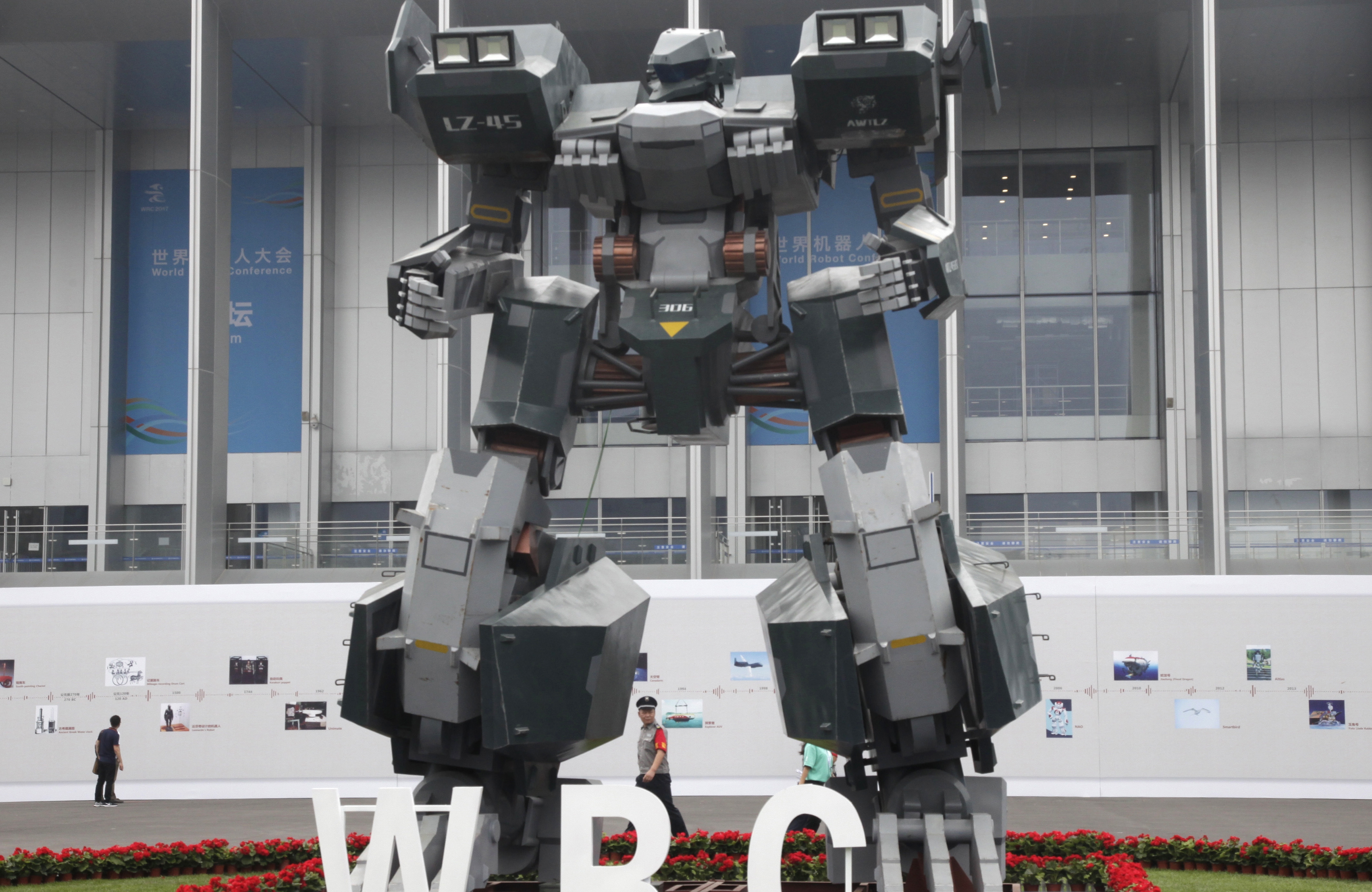 A security guard walks past a giant robot displayed at the World Robot Conference held in Beijing, China, Tuesday, Aug. 22, 2017. The annual conference is a showcase of China's burgeoning robot industry ranging from companion robots to those deployed on manufacturing assembly line and entertainement.  (AP Photo/Fu Ting)