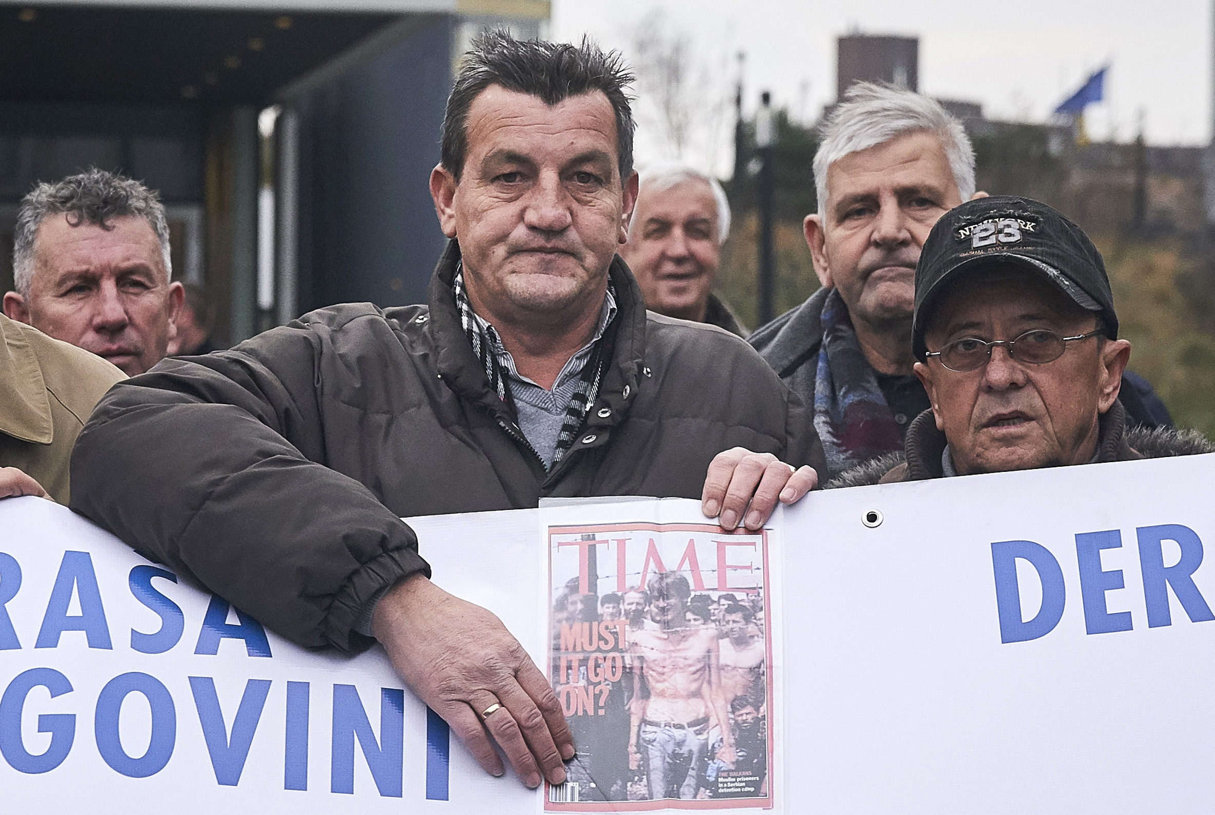 Fikret Alic, center, holds holds a copy of a magazine bearing his image, outside the Yugoslav War Crimes Tribunal, ICTY, as he waits for the verdict to be handed down in the genocide trial against former Bosnian Serb military chief Ratko Mladic, in The Hague, Netherlands, Wednesday Nov. 22, 2017. Alic, a Bosnian man who became a figurehead for the suffering of Bosnians during the war when he was photographed as an emaciated prisoner behind the wire of a Bosnian Serb prison camp, was among those waiting to watch the hearing. (AP Photo/Phil Nijhuis)