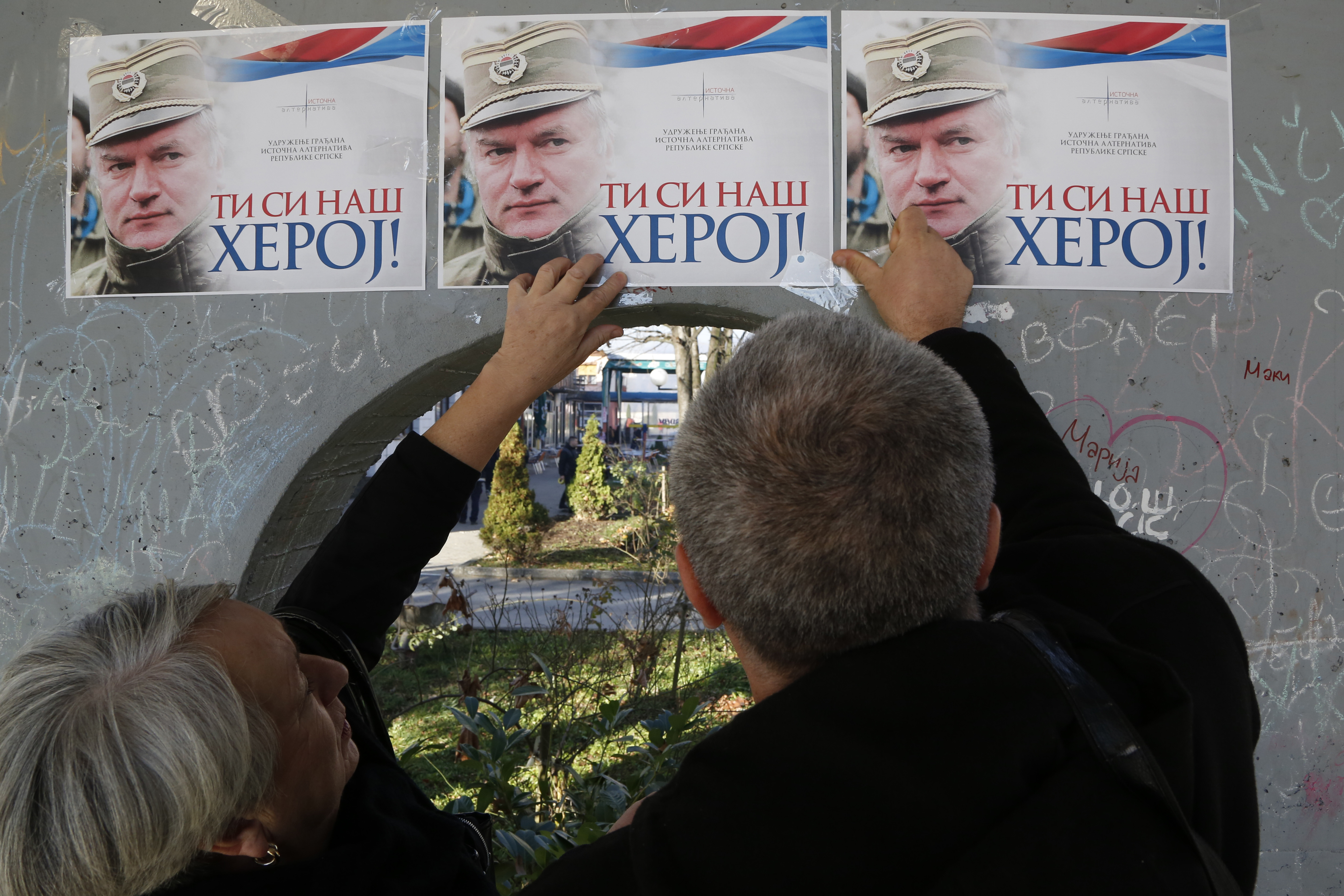 People attach posters of former Bosnian Serb military chief Ratko Mladic on a wall in Bratunac, Bosnia, Wednesday, Nov. 22, 2017. The Yugoslav War Crimes Tribunal in the The Hague is scheduled to hand down the verdict in the genocide case against former Bosnian Serb military chief Ratko Mladic on Wednesday. (AP Photo/Amel Emric)