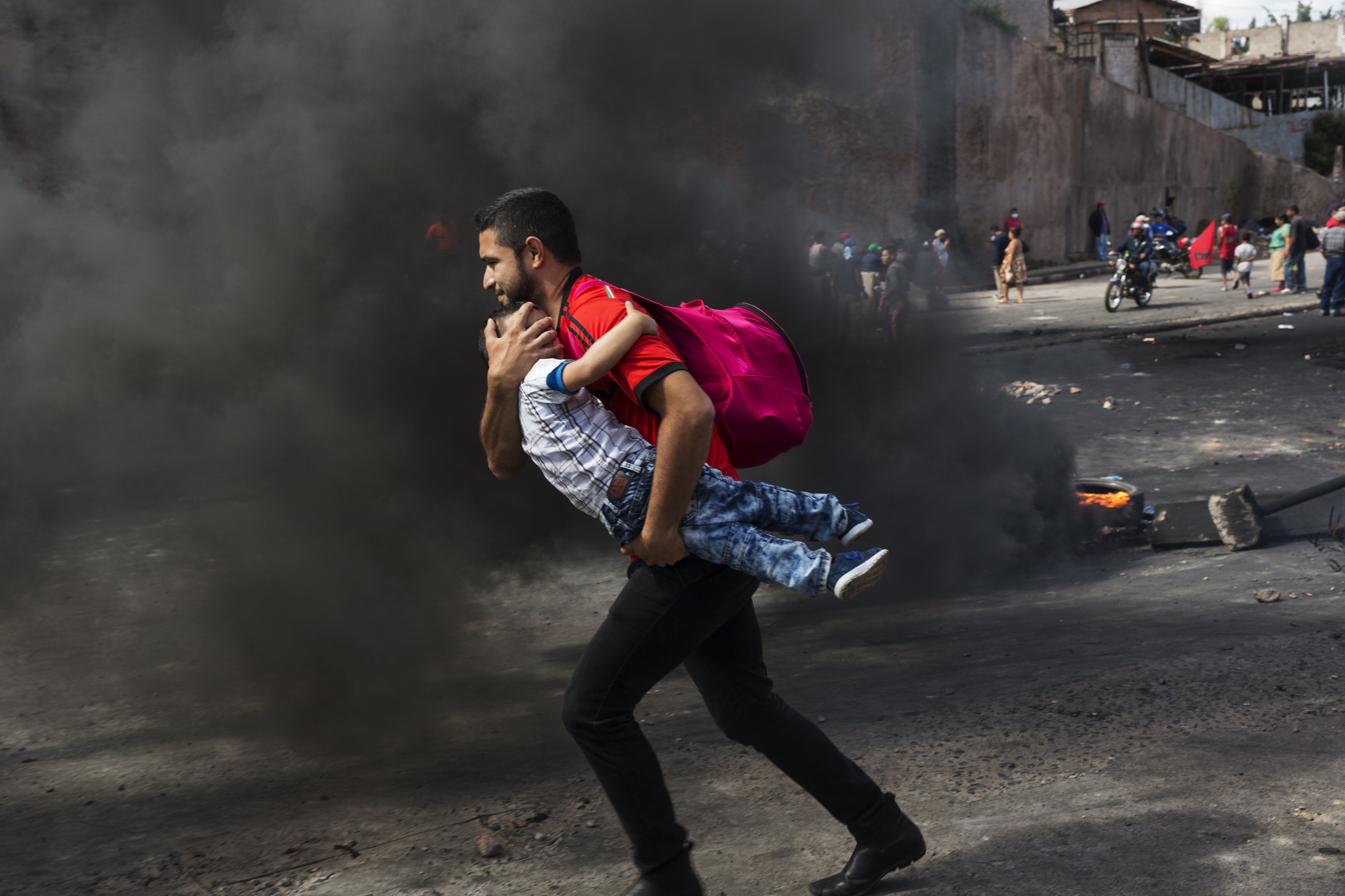 A man carries his son while crossing a burning barricade erected by supporters of presidential candidate Salvador Nasralla protesting official election results that have trickled out giving incumbent President Juan Orlando Hernandez a growing lead, in Tegucigalpa, Honduras, Friday, Dec. 1, 2017. The opposition candidate, who saw his five point lead evaporate, says he will not recognize an official vote count by the country's electoral court and is alleging manipulation of Sunday's election. (AP Photo/Rodrigo Abd)