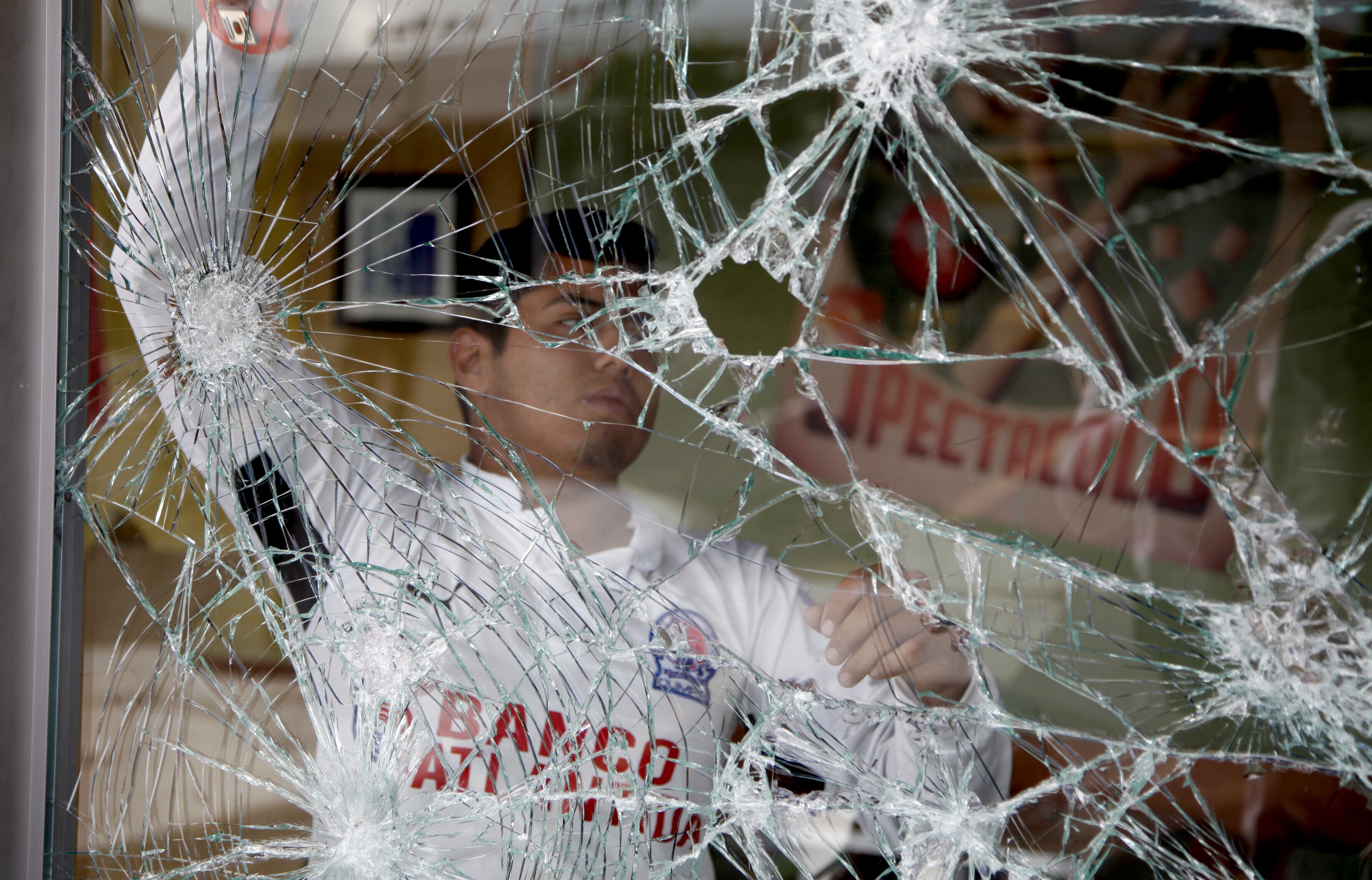 A worker of a fast food restaurant stands behind a storefront window shattered by looters, in Tegucigalpa, Honduras, Friday, Dec. 1, 2017. Protests continue in Honduras Friday as incumbent President Juan Orlando Hernandez's lead for re-election continues to grow. (AP Photo/Fernando Antonio)
