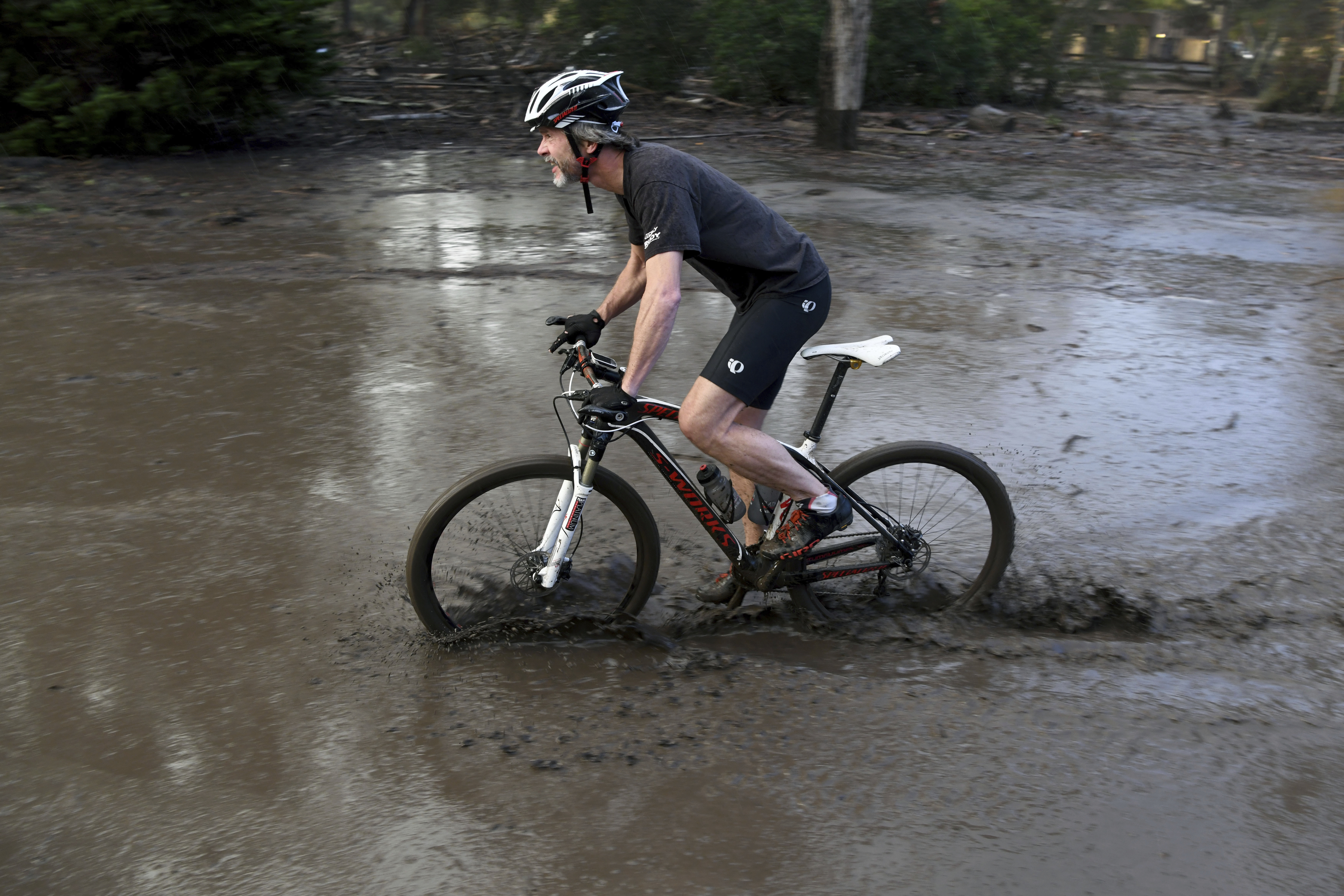 A man who gave his name only as Ian rides his bike through a mud puddle in Montecito, Calif., Tuesday, Jan. 9, 2018. More than a dozen people were killed and homes were torn from their foundations Tuesday as downpours sent mud and boulders roaring down hills stripped of vegetation by a wildfire that raged in Southern California last month. (AP Photo/Michael Owen Baker)