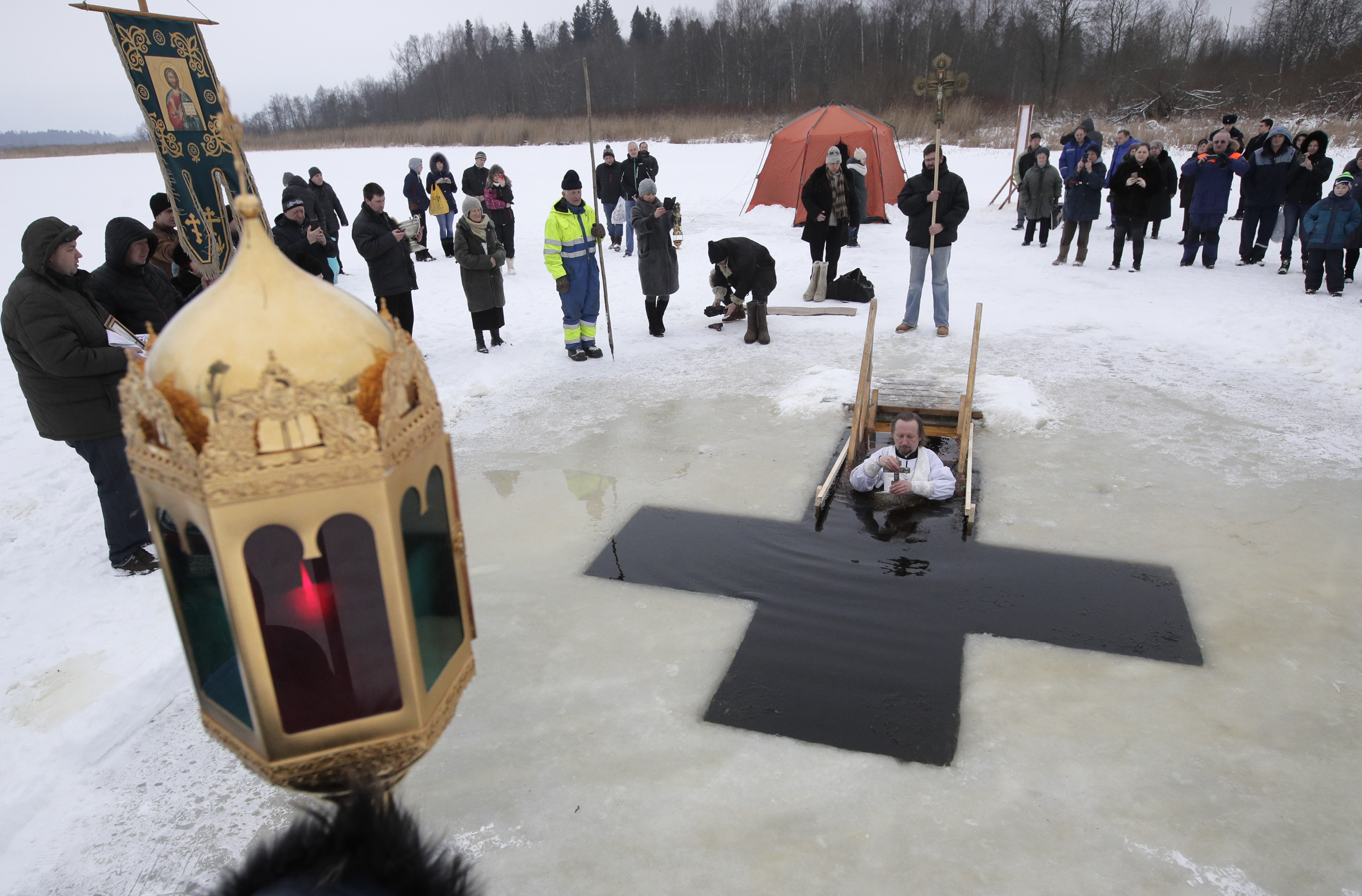 A Russian Orthodox priest conducts a service in the icy water on Epiphany at a hole in the form of Orthodox Cross at a lake in Orlino village, 70 kilometers (43 miles) south of St.Petersburg, Russia, Friday, Jan. 19, 2018. Thousands of Russian Orthodox Church followers plunged into icy rivers and ponds across the country to mark Epiphany, cleansing themselves with water deemed holy for the day. (AP Photo/Dmitri Lovetsky)
