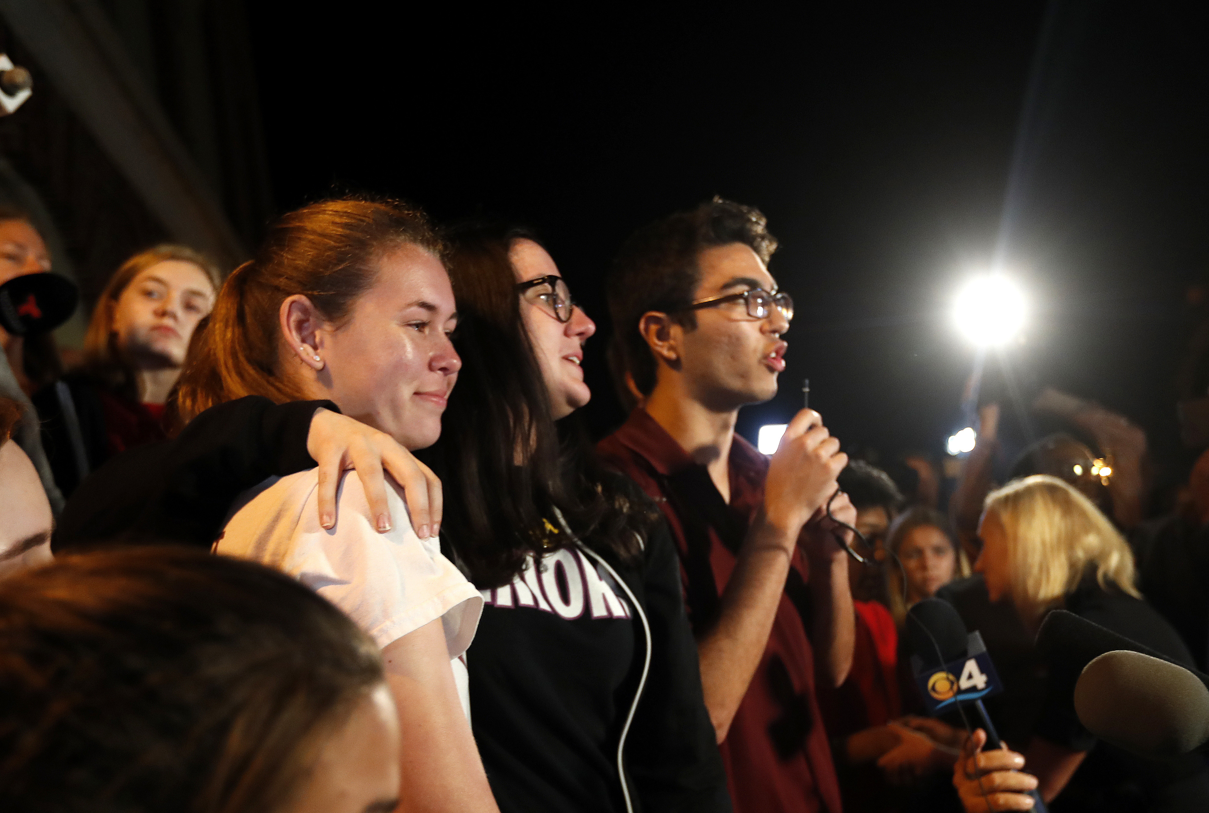 Diego Pfeiffer, a student survivor from Marjory Stoneman Douglas High School, where 17 students and faculty were killed in a mass shooting on Wednesday, speaks to a crowd of supporters and media, while fellow survivors Sophie Whitney, left, and Sarah Chadwick embrace after they arrived at Leon High School, in Tallahassee, Fla., Tuesday, Feb. 20, 2018. The students arrived in the state's capital to talk to legislators and rally for gun control reform. (AP Photo/Gerald Herbert)