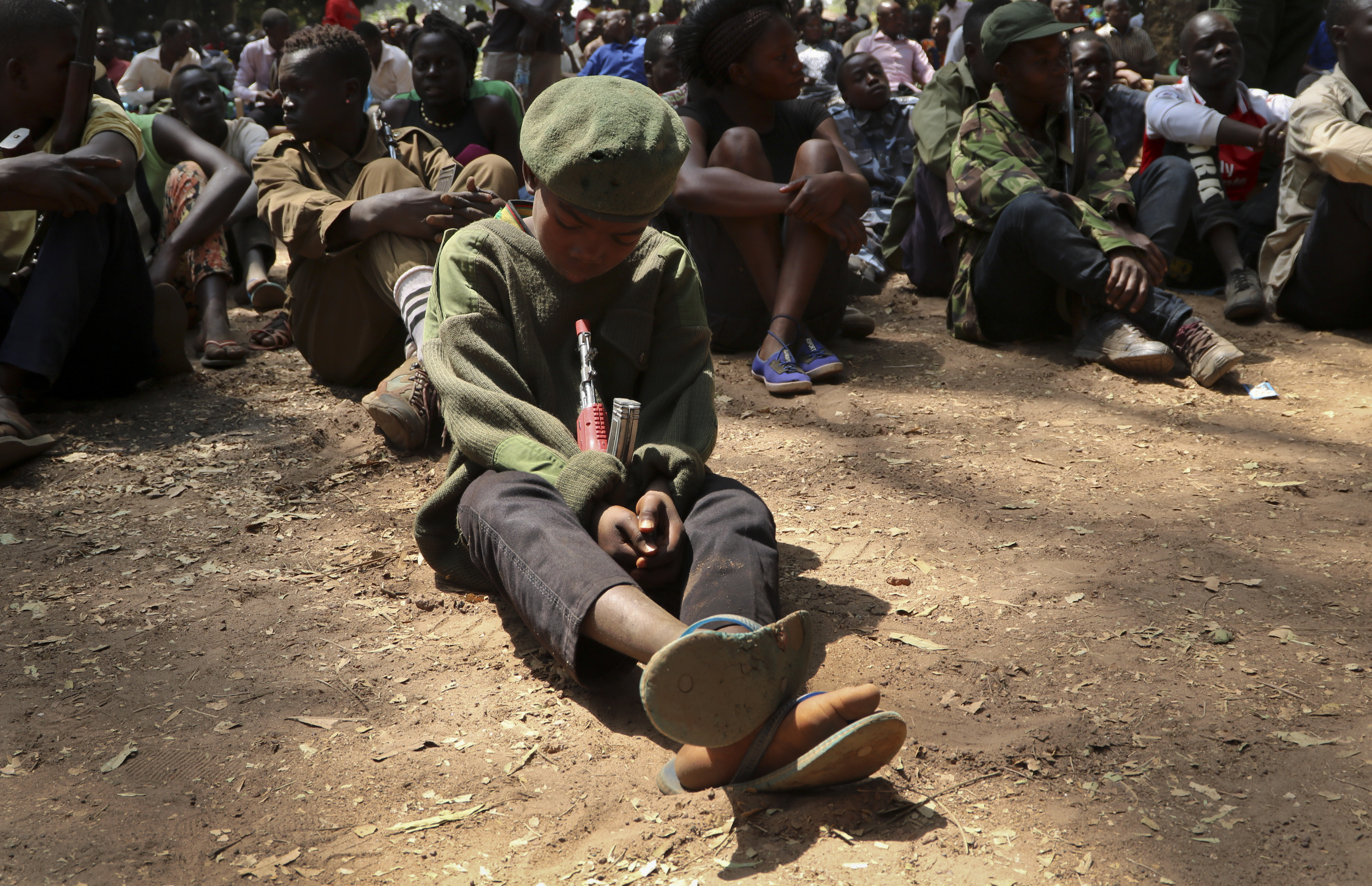 A young child soldier sits on the ground at a release ceremony, where he and others laid down their weapons and traded in their uniforms to return to 