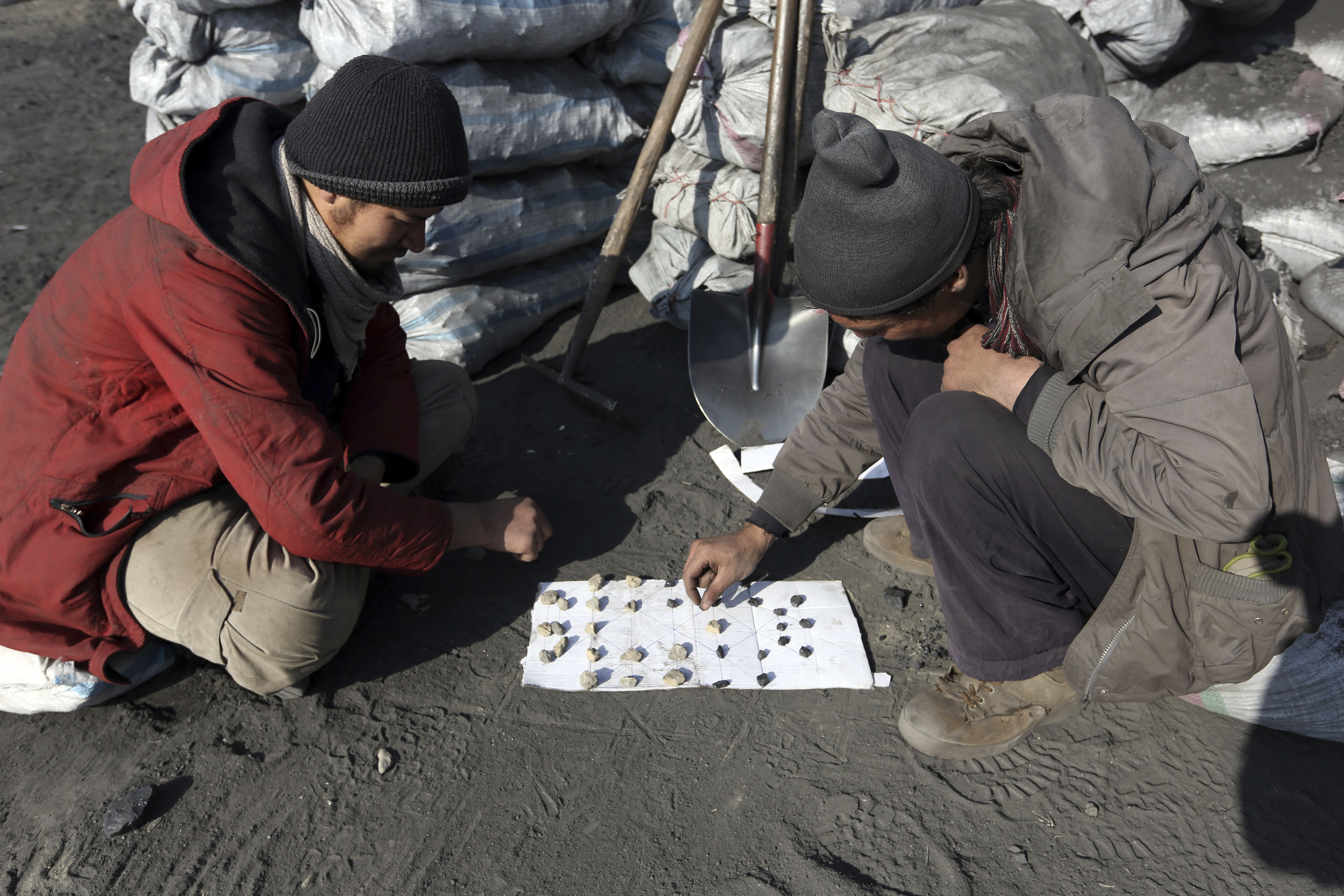 Afghan laborers play a game at a charcoal market in Dehsabz district of Kabul, Afghanistan Tuesday, Dec. 5, 2017. In winter, prices of wood and charcoal rise among all other necessities for Afghans. (AP Photo/Rahmat Gul)