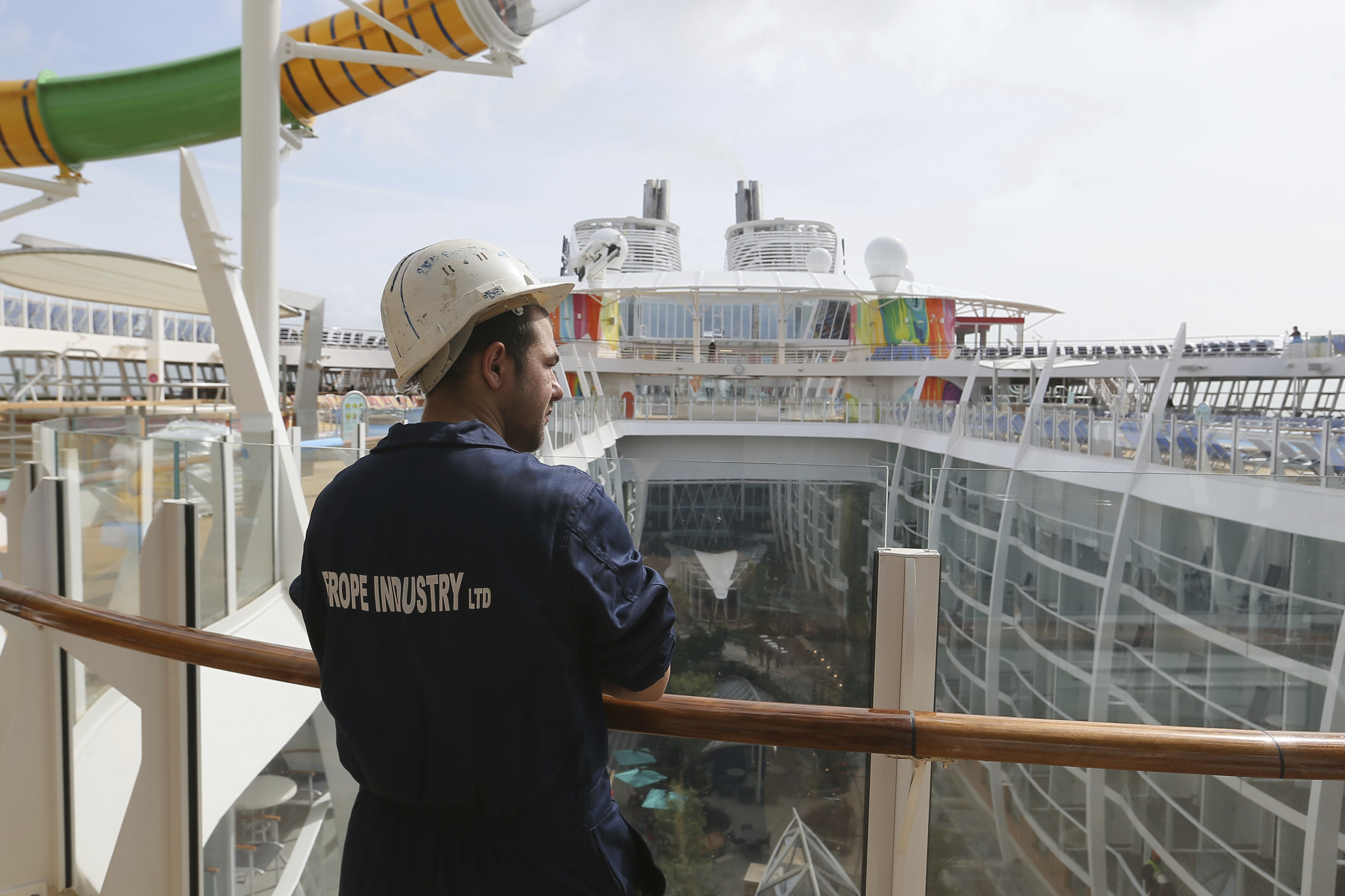 A worker watches The Symphony of the Seas, the world's largest cruise ship, docking at Saint Nazaire port, western France, Friday, March 23, 2018. Royal Caribbean International took delivery of the much-awaited, 228,081-ton Symphony of the Seas from the French shipyard STX. (AP Photo/David Vincent)