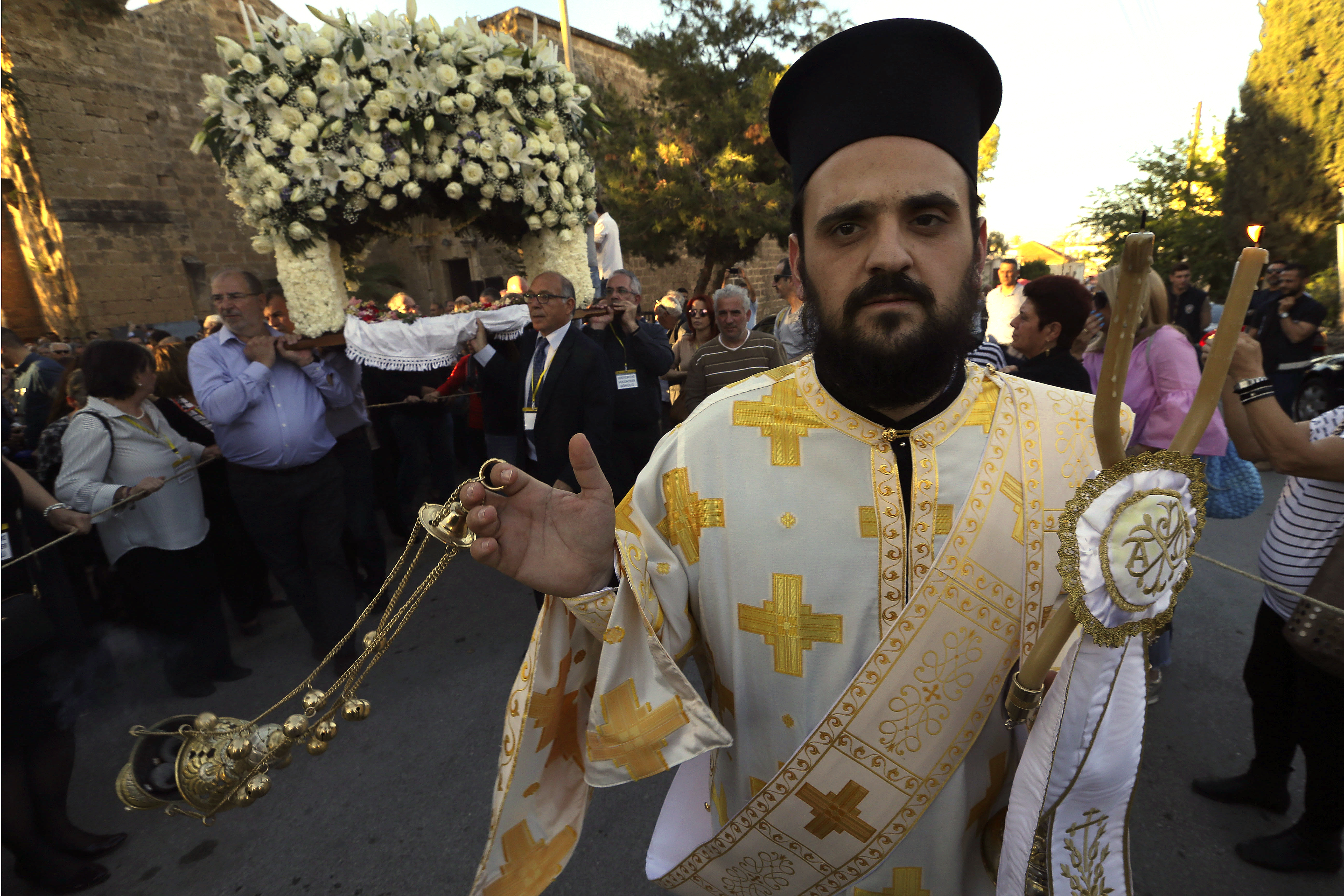A Greek Orthodox Christian Priest holds candles during the Good Friday procession of the Epitaphios, at the church of Saint George Exorinos within the ancient walls of Famagusta city, Cyprus, on Friday, April 6, 2018. According to Orthodox tradition, the faithful follow the Epitaphios which rests under a flower-adorned canopy in procession around the church to commemorate Christ's funeral procession. This is one of the few times in recent years where Turkish Cypriot authorities have permitted liturgical services at the 14th Century church since the island was divided in 1974 when Turkey invaded following a coup by supporters of union with Greece. (AP Photo/Petros Karadjias)