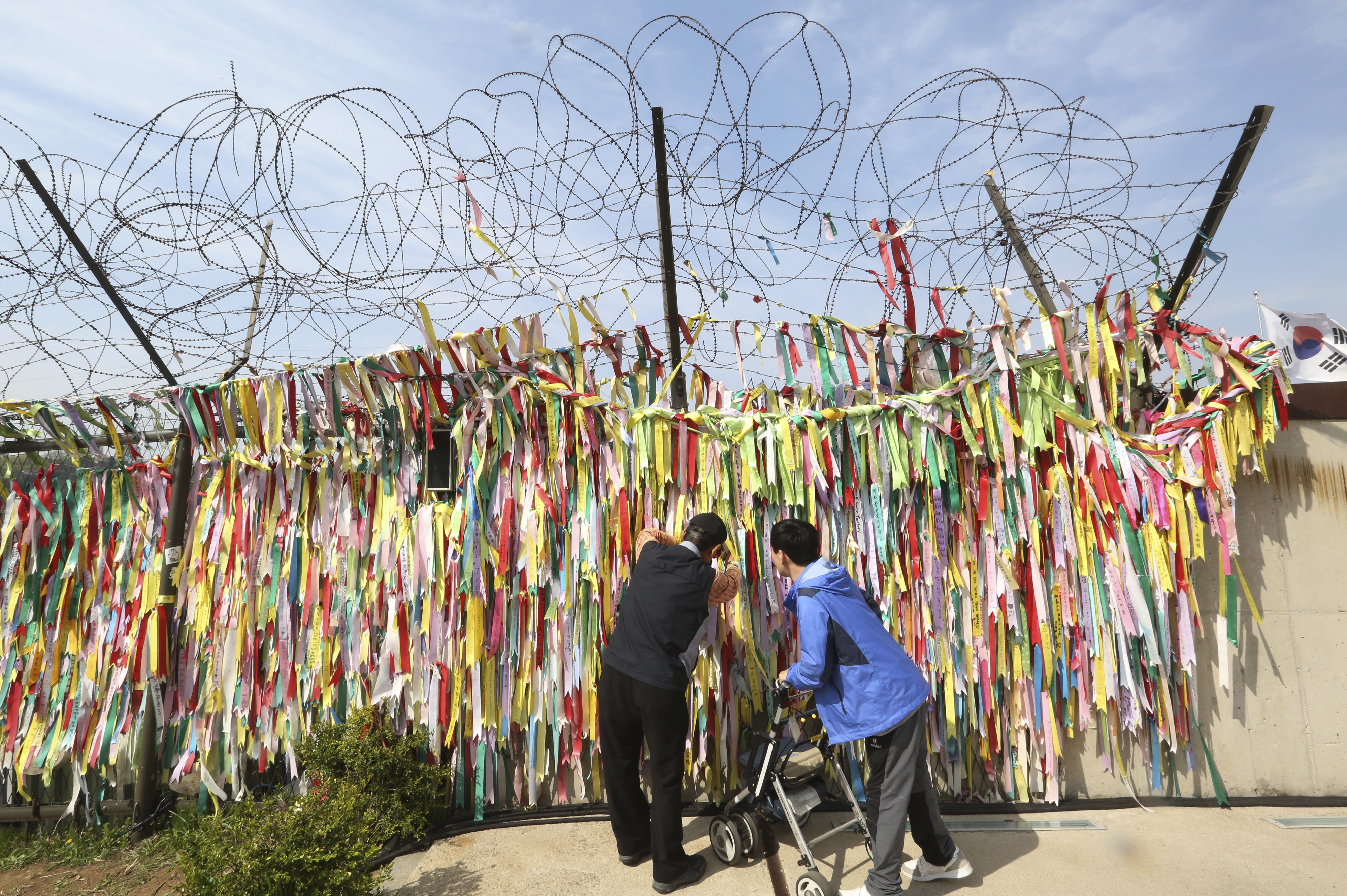 A man hangs a ribbon carrying messages wishing the reunification and peace of the two Koreas on the wire fence at the Imjingak Pavilion in Paju, near the border with North Korea, South Korea, Thursday, April 26, 2018. North Korean leader Kim Jong Un and South Korean President Moon Jae-in will plant a commemorative tree and inspect an honor guard together after Kim walks across the border Friday for their historic summit, Seoul officials said Thursday. (AP Photo/Ahn Young-joon)