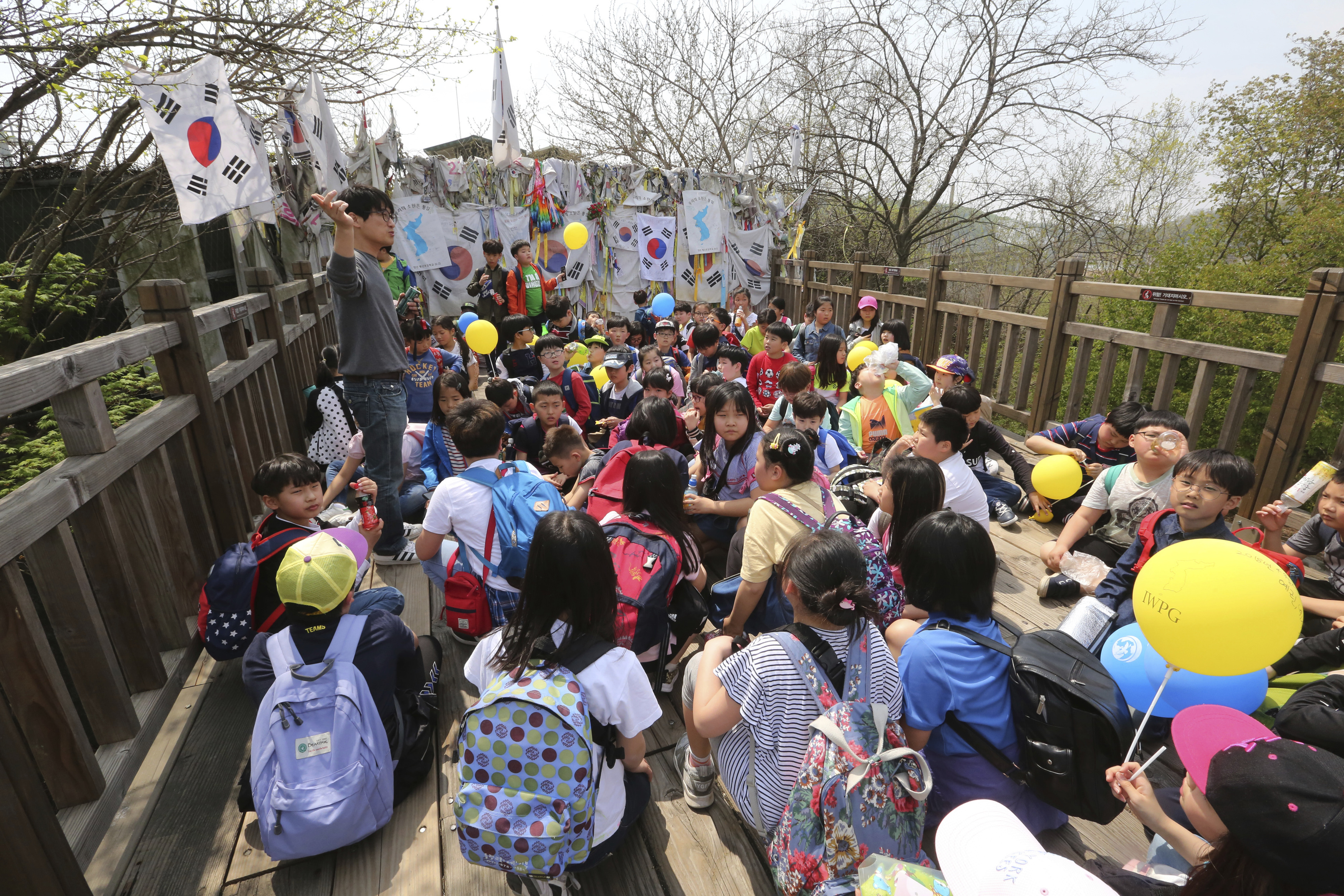 An elementary school teacher, left top, explains about the upcoming summit between South and North Korea to his students in front of a barbed wire fence with messages wishing for the reunification of the two Koreas at the Imjingak Pavilion in Paju, South Korea, near the border with North Korea, Thursday, April 26, 2018. North Korean leader Kim Jong Un and South Korean President Moon-Jae-in will plant a commemorative tree and inspect an honor guard together after Kim walks across the border Friday for their historic summit, Seoul officials said Thursday. (AP Photo/Ahn Young-joon)