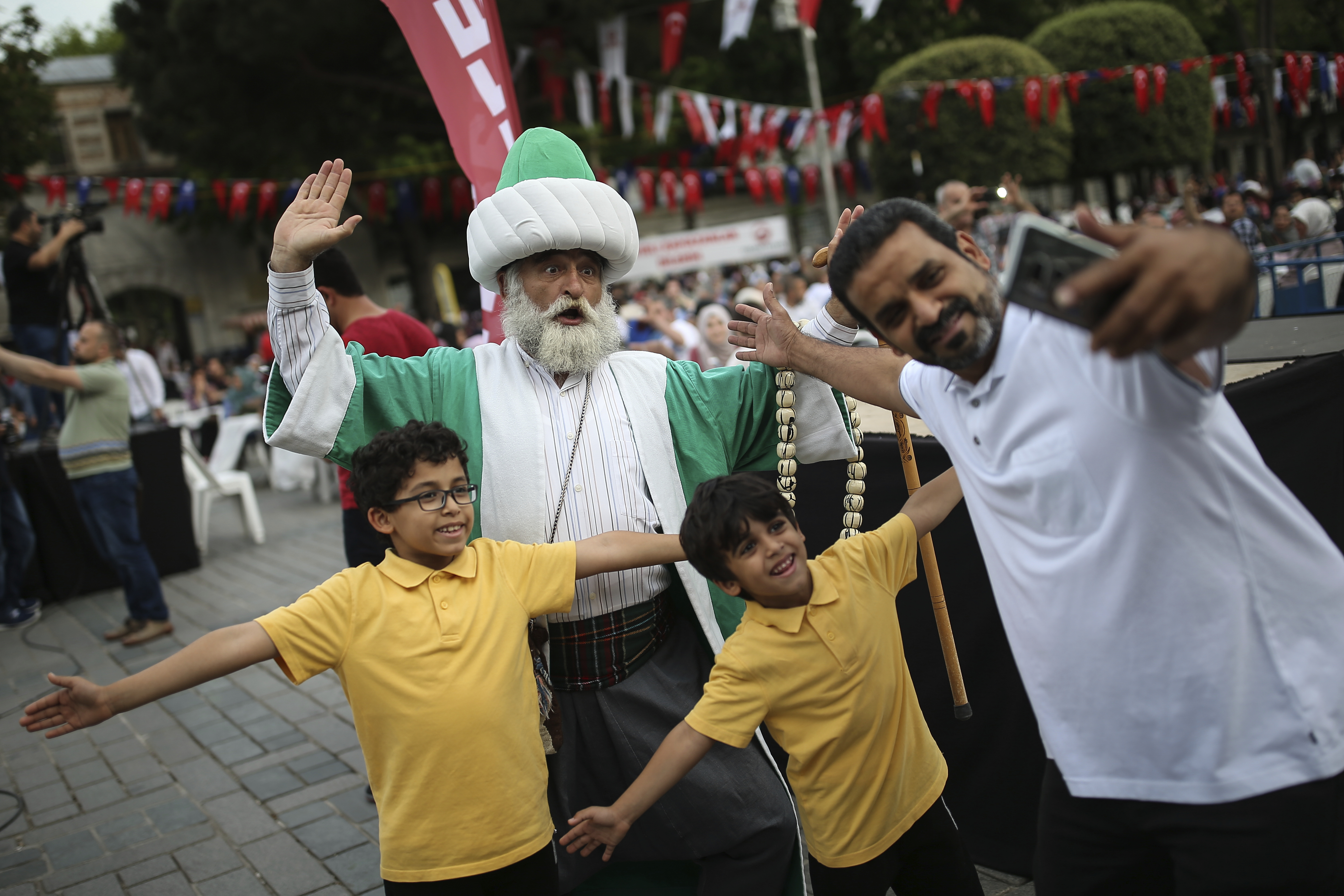 A man in Ottoman attire poses for pictures with a family as people prepare to break their fast in the historic Sultanahmet district of Istanbul, Wednesday, May 16, 2018 on the first day of the fasting month of Ramadan. Muslims throughout the world are marking Ramadan - a month of fasting during which the observants abstain from food, drink and other pleasures from sunrise to sunset. After an obligatory sunset prayer, a large feast known as 'iftar' is shared with family and friends. (AP Photo/Emrah Gurel)