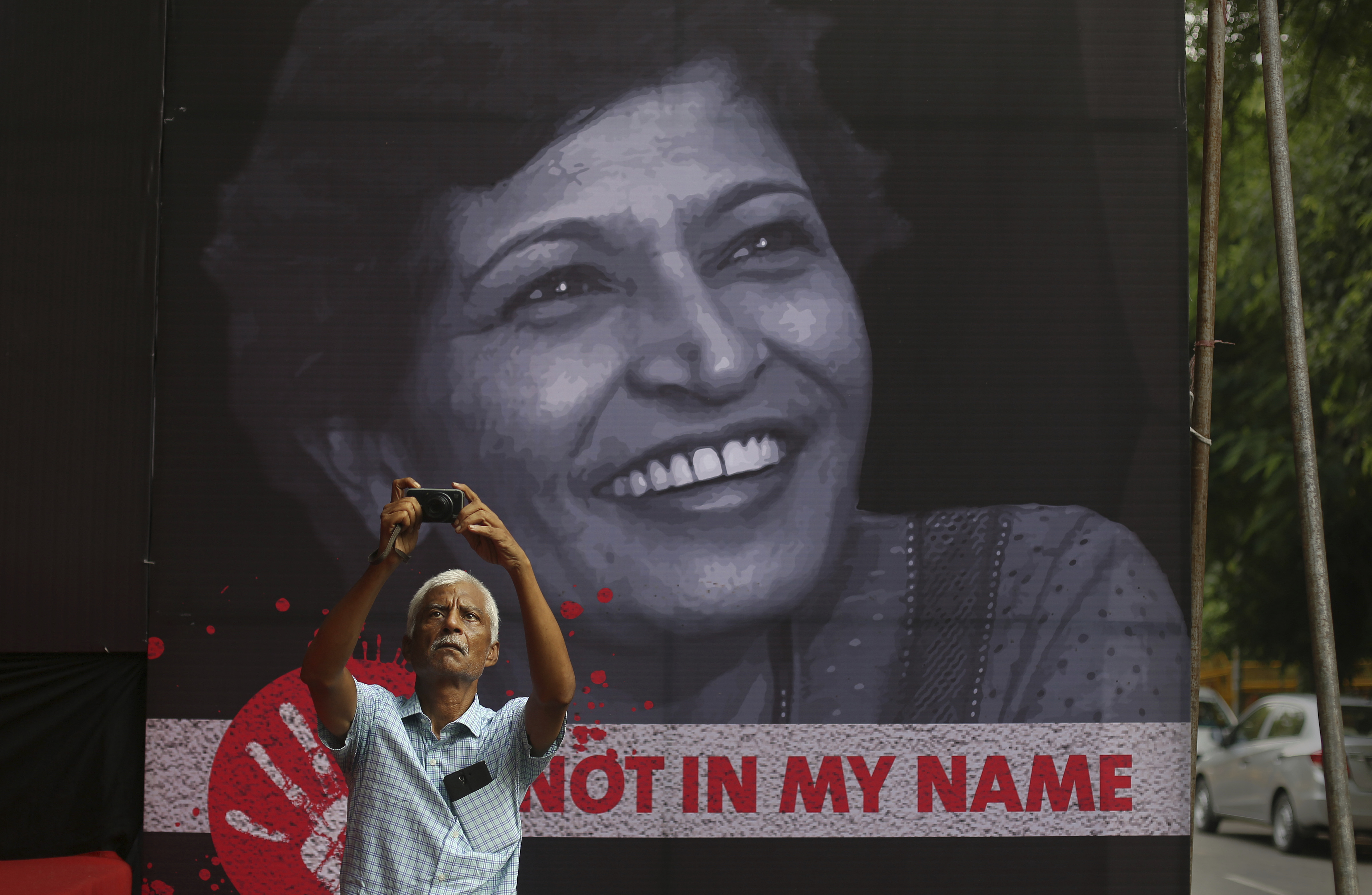 An Indian man takes a photographs during a protest condemning the killing of journalist Gauri Lankesh, protrait in background, in New Delhi, India, Thursday, Sept. 7, 2017. Lankesh's killing has provoked outrage and anguish across the country, with thousands protesting what they see as an effort to silence critics of India's ruling Hindu nationalist party. (AP Photo/Altaf Qadri)