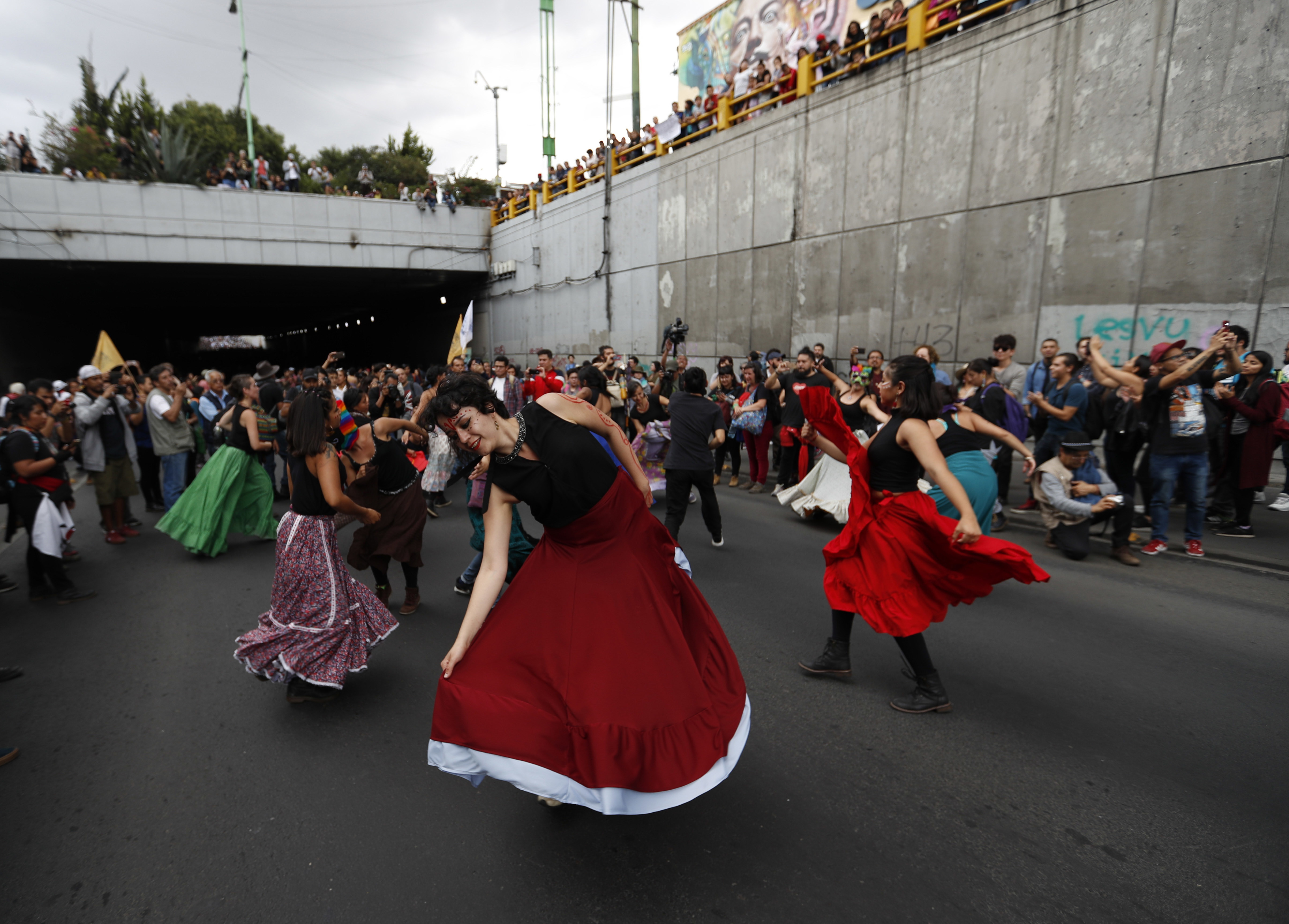 Demonstrators  dance during a march in remembrance of the 1968 Tlatelolco student massacre in Mexico City, Tuesday, Oct. 2, 2018. Mexico is marking the massacre of student protesters by army troops 50 years ago. The mural behind reads in Spanish: 