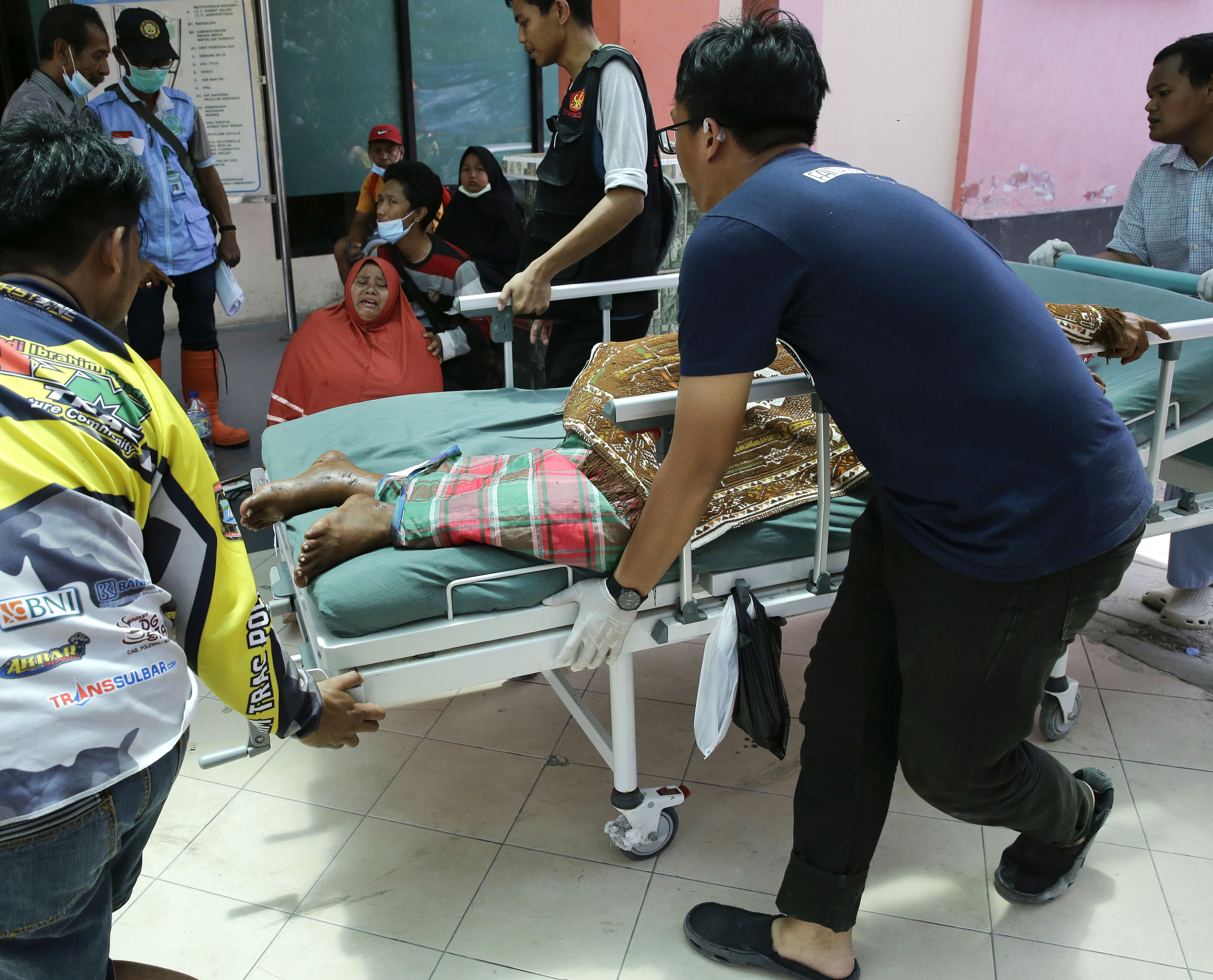 An injured man is brought to the hospital as one woman cries after learning about her daughter's death in a massive earthquake and tsunami in Palu, Central Sulawesi, Indonesia Thursday, Oct. 4, 2018. Nearly a week after a magnitude 7.5 quake spawned a deadly tsunami on Indonesia’s island of Sulawesi, countless people have yet to find their loved ones _ both survivors and the dead. As of Thursday, the official death toll was 1,424, with 113 people missing. Many families, though, never registered their losses with police, and others have failed to identify them before they were buried anonymously in mass graves.(AP Photo/Aaron Favila)