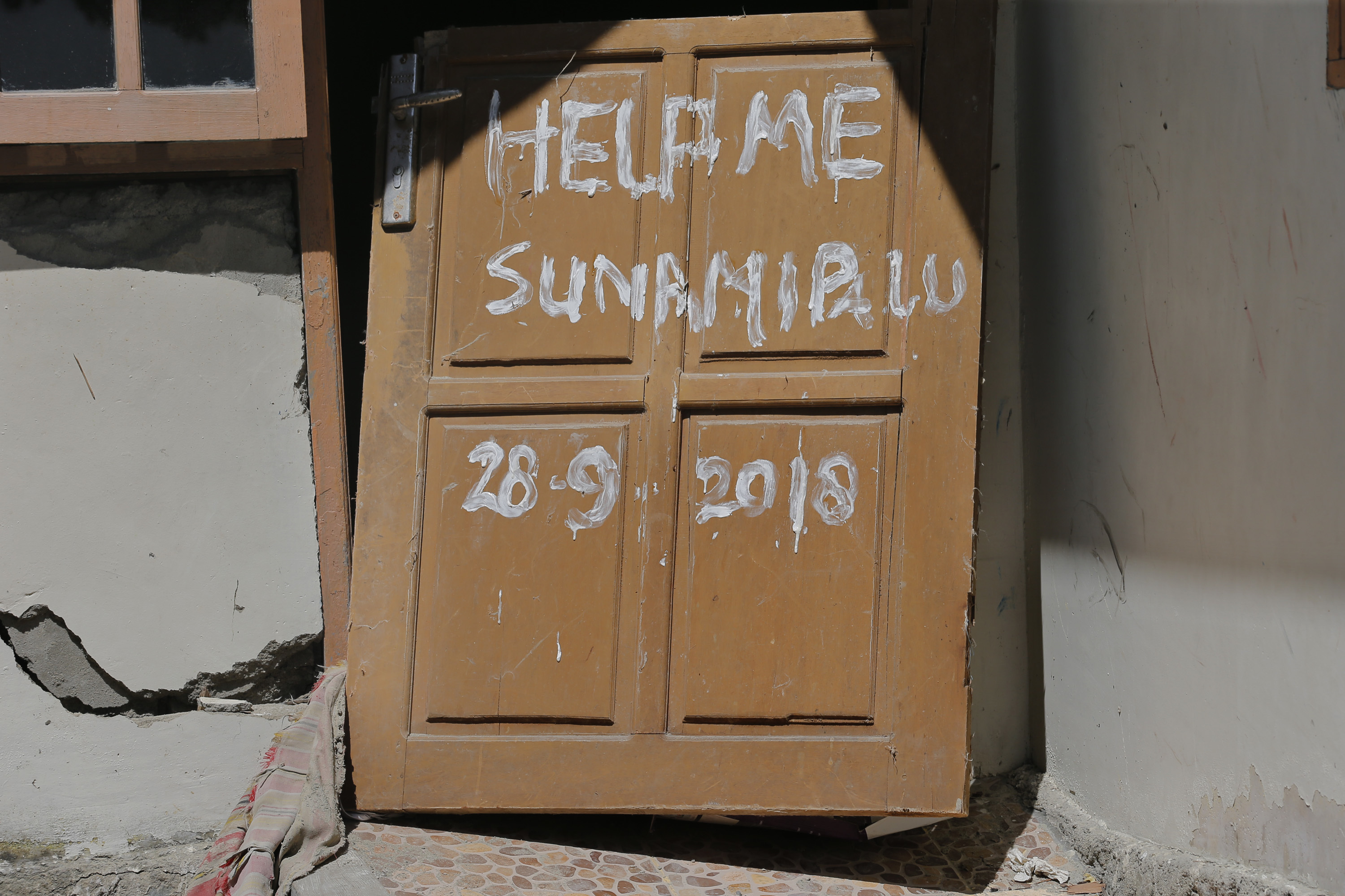 A message is written on the door of a house damaged by the massive earthquake and tsunami in Loly, Central Sulawesi, Indonesia Friday, Oct. 5, 2018. French rescuers say they've been unable to find the possible sign of life they detected a day earlier under the rubble of a hotel that collapsed in the earthquake a week ago on Indonesia's Sulawesi island. (AP Photo/Tatan Syuflana)