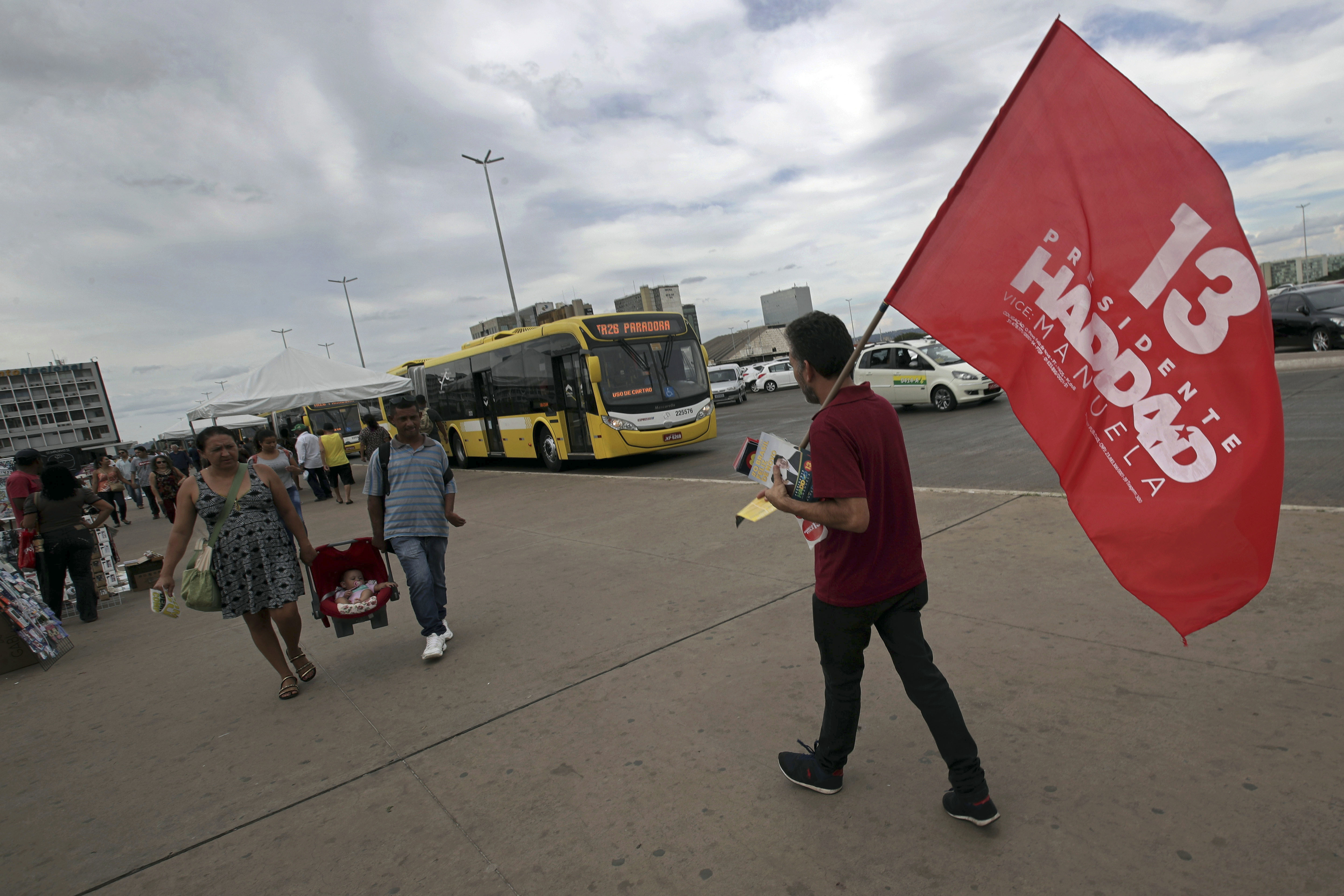 A lonely supporter of Workers' Party presidential candidate Fernando Haddad walks with a campaign flag, at a bus station in Brasília, Brazil, Wednesday, Oct. 17, 2018. Before the run-off election in Brazil on 28 October, right-wing populist presidential candidate Jair Bolsonaro is showing a clear advantage over Haddad. (AP Photo/Eraldo Peres)