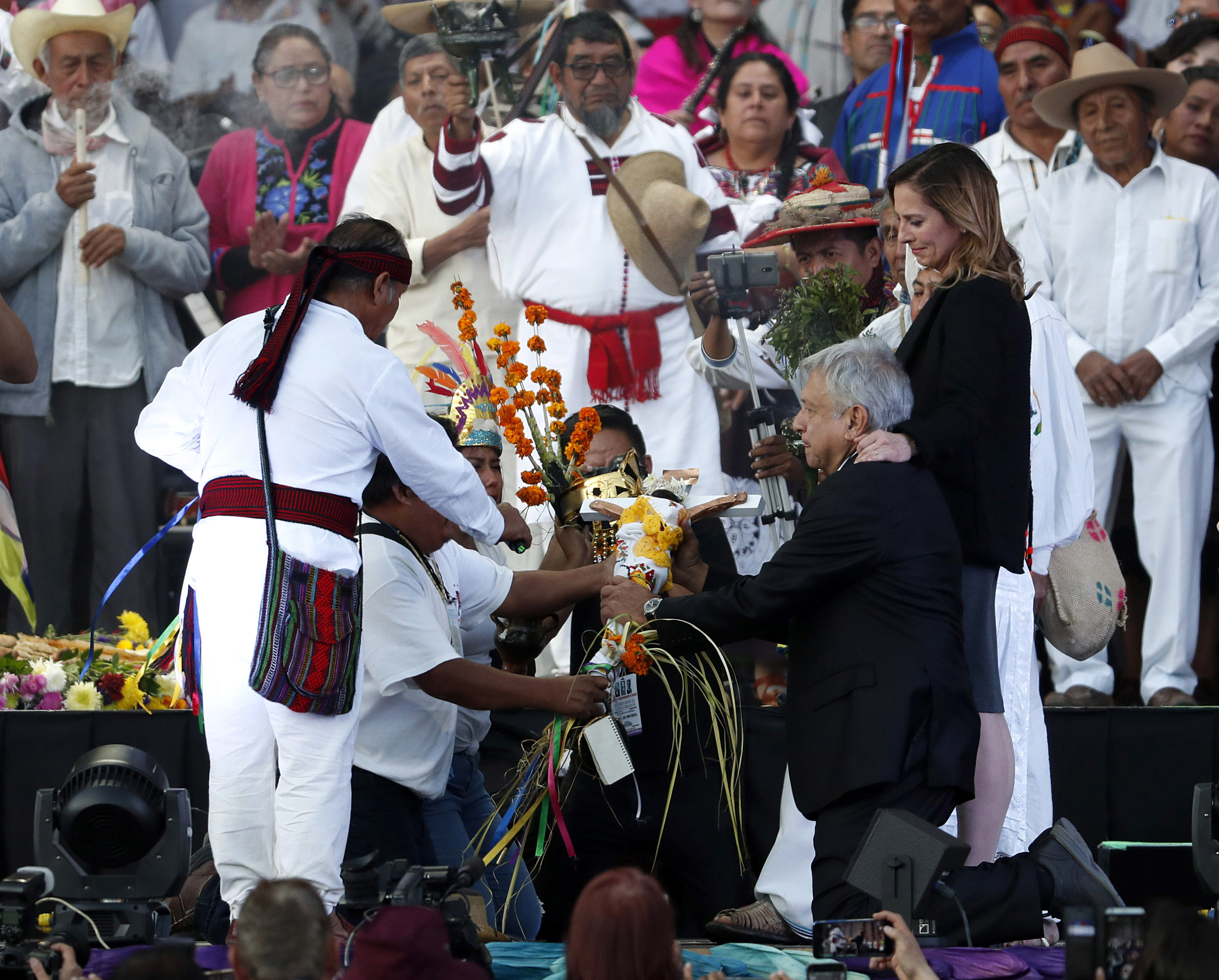 Kneeling next to his wife Beatriz Gutierrez Muller, right center, Mexico's new President Andres Manuel Lopez Obrador is given a cross during a traditional indigenous ceremony at the Zocalo, in Mexico City, Saturday, Dec. 1, 2018. Lopez Obrador was formally anointed leader by indigenous groups at the ceremony. (AP Photo/Moises Castillo)