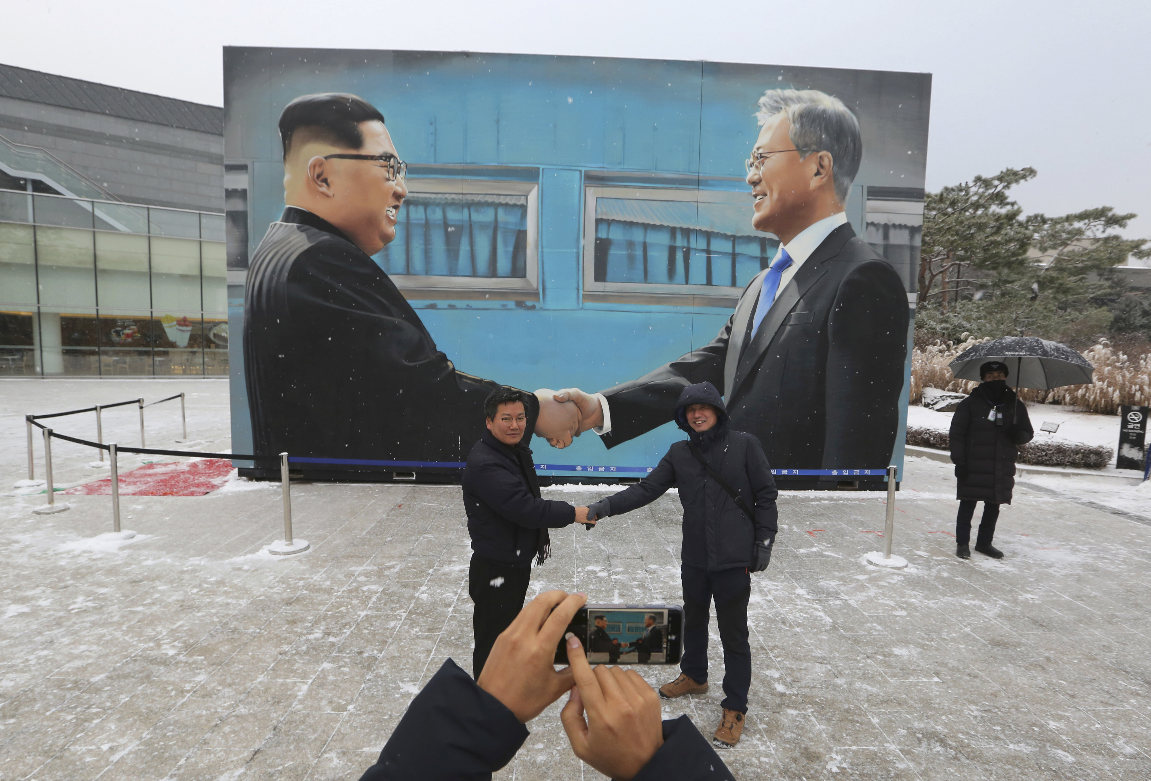 Two men pose with an image of North Korean leader Kim Jong Un, left, and South Korean President Moon Jae-in displayed at a park near the presidential Blue House in Seoul, South Korea, Thursday, Dec. 13, 2018. Kim's return visit to Seoul appears unlikely to take place this month, a senior South Korean official said. (AP Photo/Ahn Young-joon)