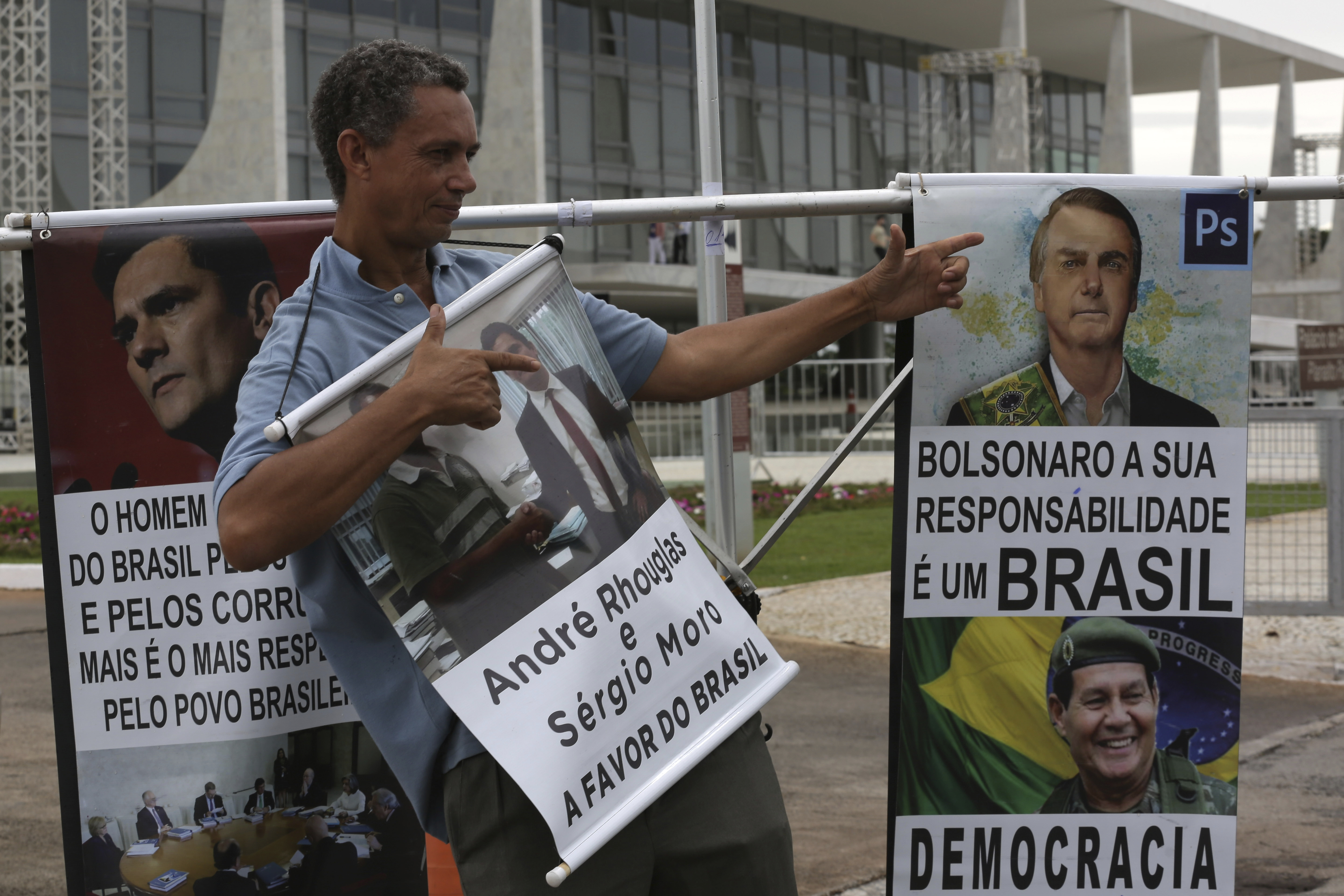 Andre Rhouglas, a supporter of Brazil's President-elect Jair Bolsonaro, flashes finger guns in front of posters featuring Bolsonaro and Vice President-elect Gen. Hamilton Mourao, in front of the Planalto Presidential Palace, in Brasilia, Brazil, Friday, Dec. 28, 2018. The Secretary of Public Security in Brasilia said that they are expecting as many as 500,000 people to attend the presidential inaugural festivities. Brazil's military has deployed anti-aircraft missiles and fighter jets to protect the event from the air. On the ground, more than 3,000 police and military will take to the streets. (AP Photo/Eraldo Peres)