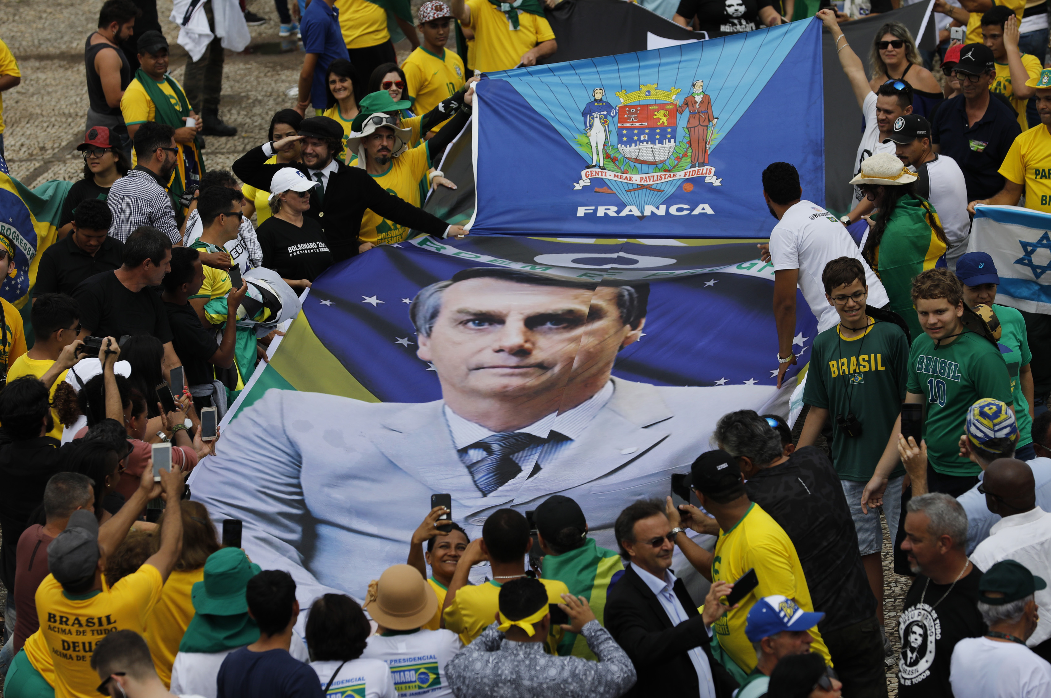 People hold a banner with a photo of Brazil's former army captain Jair Bolsonaro before the swearing-in ceremony, in front of the Planalto palace in Brasilia, Brail, Tuesday Jan. 1, 2019.  Once an outsider mocked by fellow lawmakers for his far-right positions, constant use of expletives and even casual dressing, Bolsonaro is taking office as Brazil's president Tuesday. (AP Photo/Silvia Izquierdo)