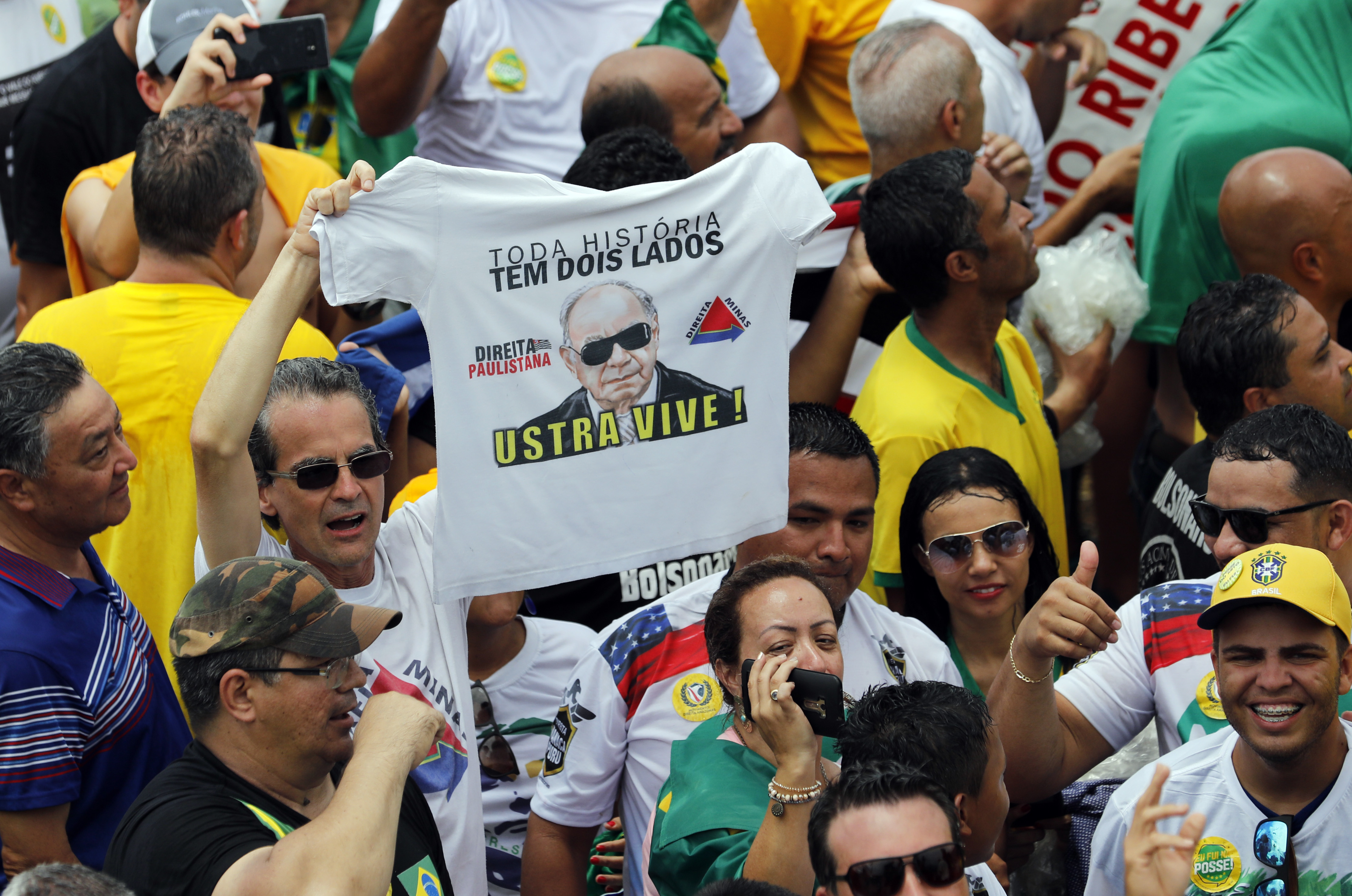 A supporter of Brazil's President Elect Jair Bolsonaro holds a T-shirt with the image of former army officer and right wing politician Carlos Alberto Brilhante Ustra, prior Bolsonaro's inauguration, in Brasilia, Brazil, Tuesday Jan. 1, 2019. Ustra, who died in 2015, became the first military official to be recognized, by a civil court in Sao Paulo, as a torturer during the military dictatorship. (AP Photo/Silvia Izquierdo)