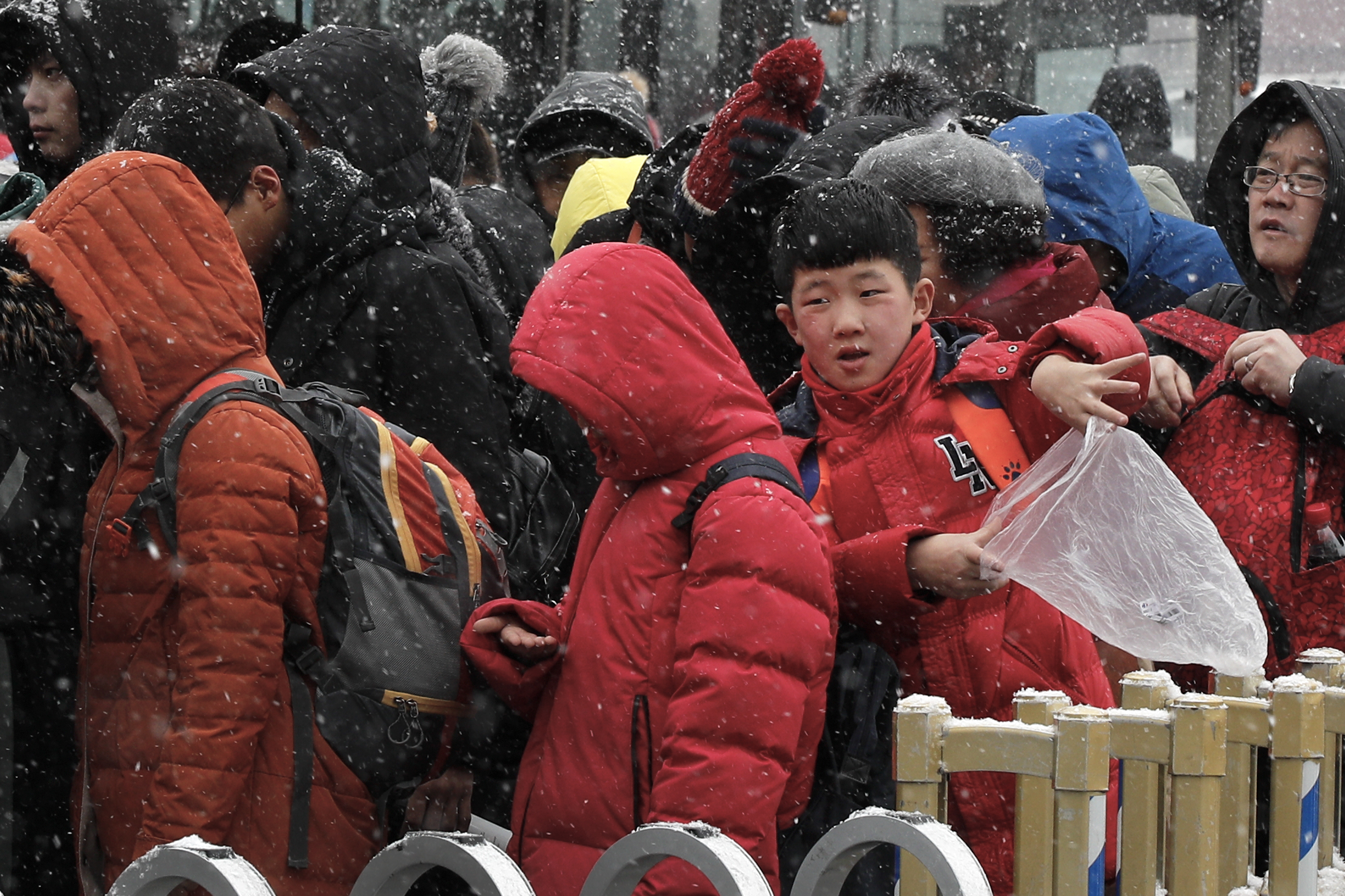 A child uses a plastic bag to catch snow as people line-up to enter the National Museum in Beijing, Tuesday, Feb. 12, 2019. China's capital is mostly dry in the winter but a storm system brought snow to the city on Tuesday morning. (AP Photo/Andy Wong)