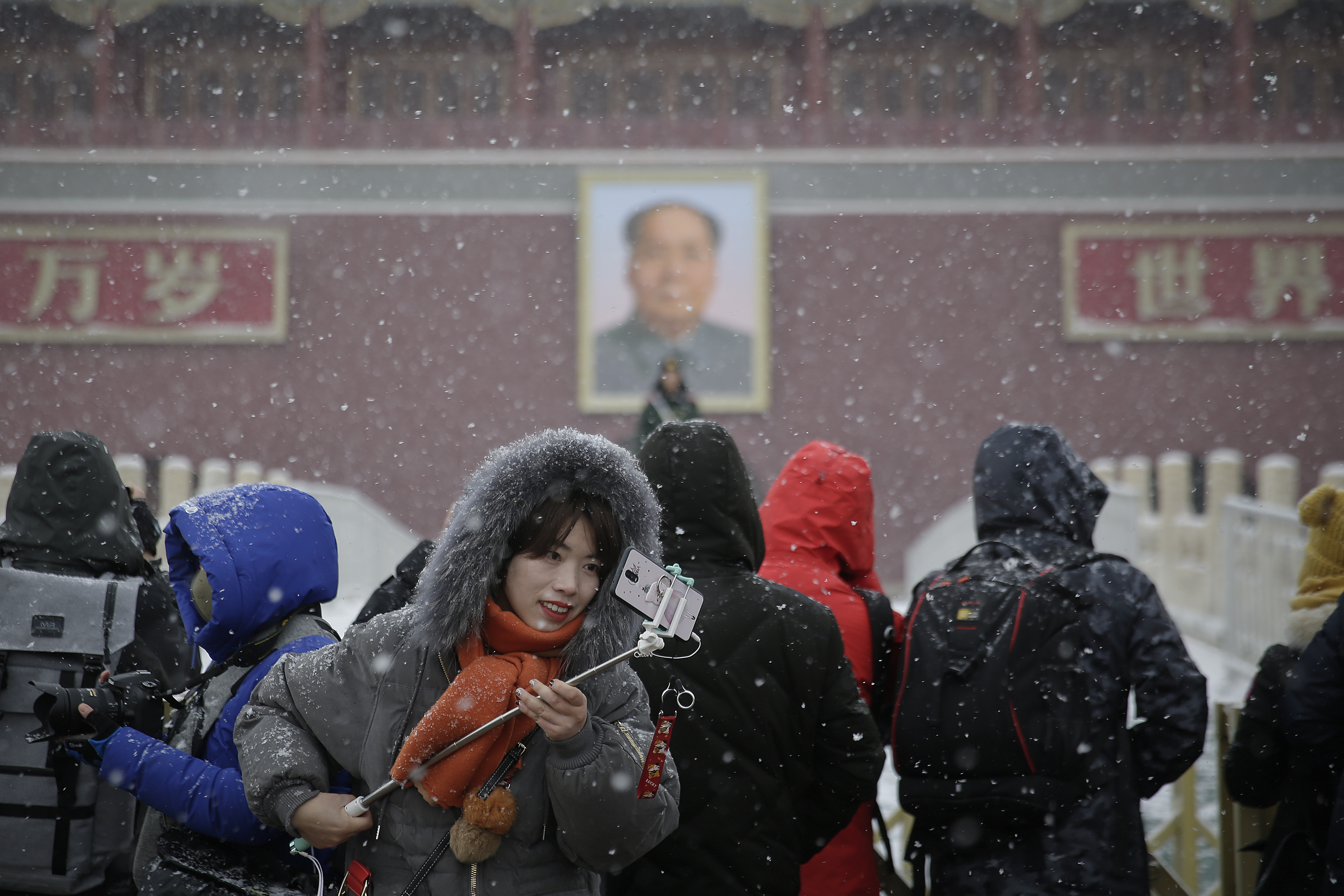A woman checks her photo as visitors takes photos of Tiananmen Gate as snow falls in Beijing, Tuesday, Feb. 12, 2019. China's capital is mostly dry in the winter but a storm system brought snow to the city on Tuesday morning. (AP Photo/Andy Wong)