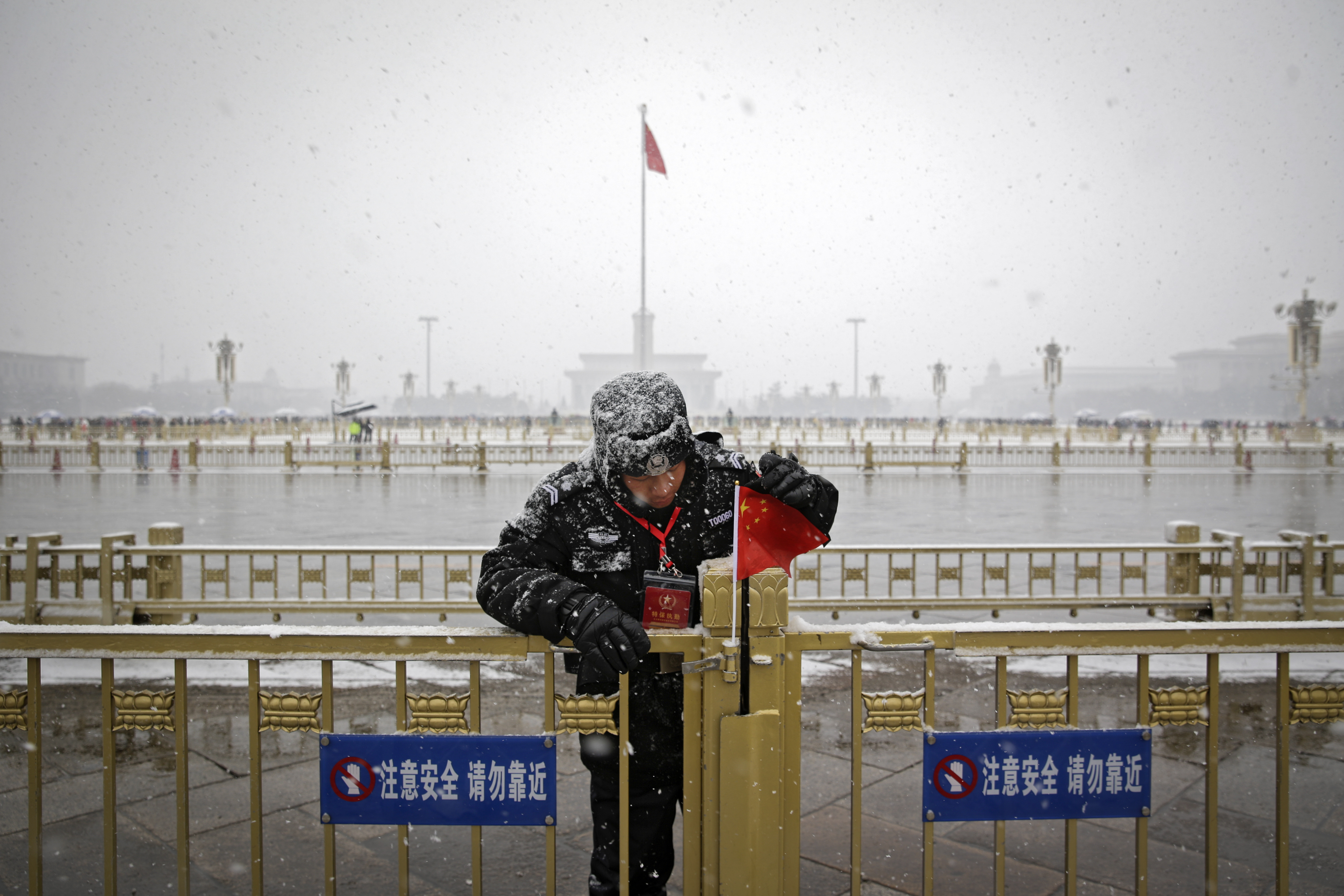 A policeman adjusts a national flag sticks on the barrier against Tiananmen Square as snow falls in Beijing, Tuesday, Feb. 12, 2019. China's capital is mostly dry in the winter but a storm system brought snow to the city on Tuesday morning. (AP Photo/Andy Wong)