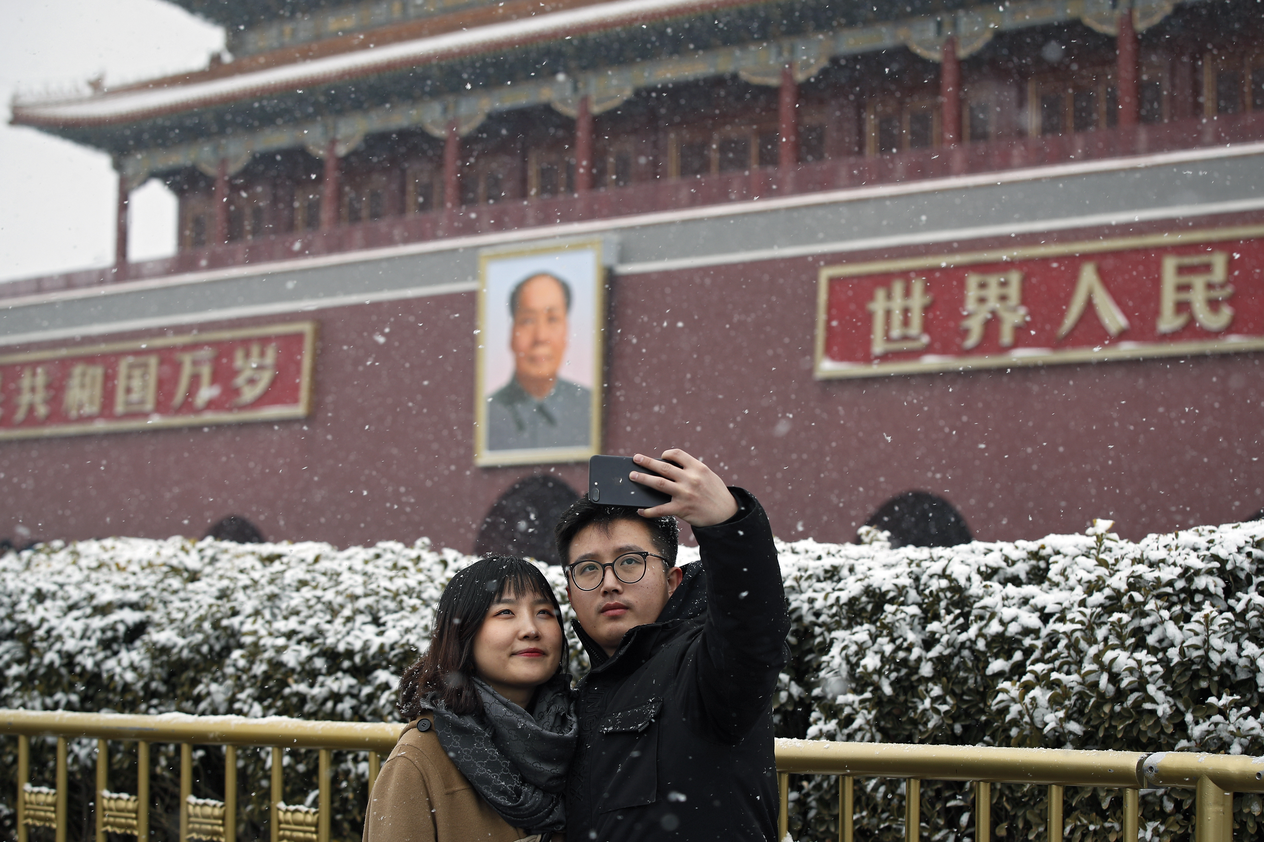 A couple takes a selfie with Tiananmen Gate as snow falls in Beijing, Tuesday, Feb. 12, 2019. China's capital is mostly dry in the winter but a storm system brought snow to the city on Tuesday morning. (AP Photo/Andy Wong)