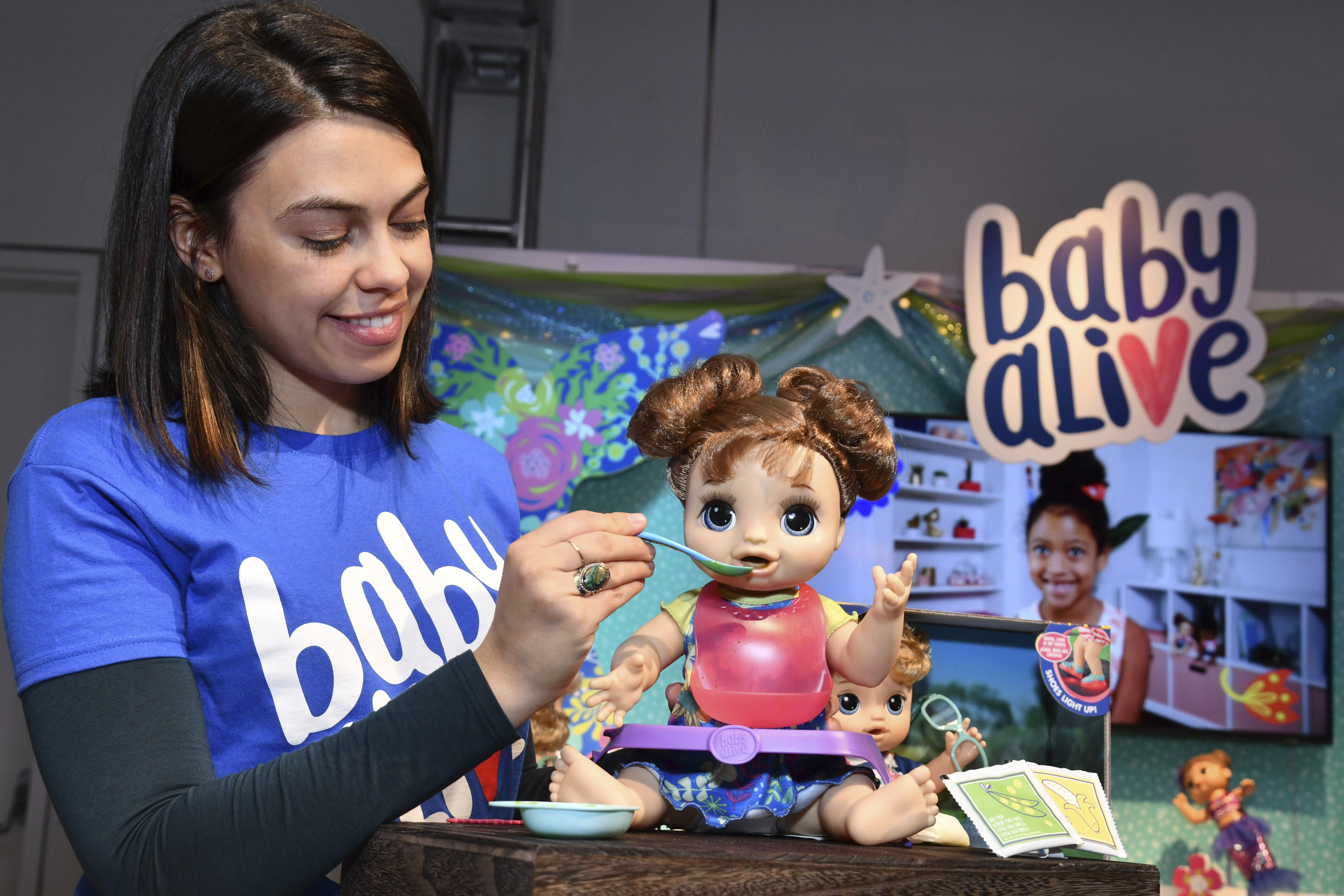 IMAGE DISTRIBUETD FOR HASBRO-  A demonstrator at the Hasbro, Inc. showroom feeds the BABY ALIVE HAPPY HUNGRY BABY Doll at the American International Toy Fair on Friday, Feb. 15, 2018 in New York. BABY ALIVE brand delivers realistic baby moments in surprising ways that allow kids to care for their doll just like a 'real parent.' (Charles Sykes/AP Images for Hasbro)