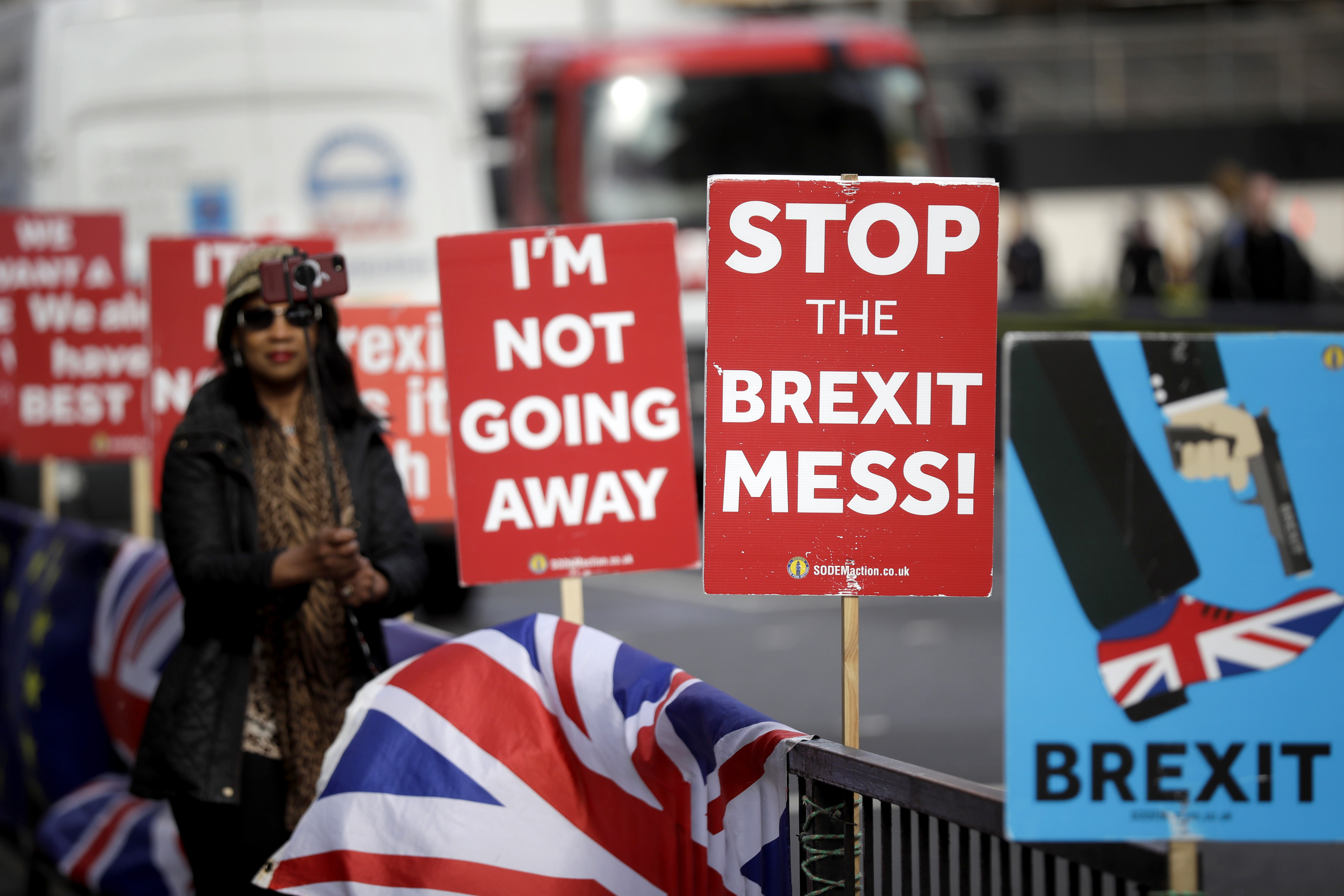 A tourist takes a selfie next to placards placed by anti-Brexit supporters stand opposite the Houses of Parliament in London, Monday, March 18, 2019. British Prime Minister Theresa May was making a last-minute push Monday to win support for her European Union divorce deal, warning opponents that failure to approve it would mean a long — and possibly indefinite — delay to Brexit. Parliament has rejected the agreement twice, but May aims to try a third time this week if she can persuade enough lawmakers to change their minds. (AP Photo/Matt Dunham)