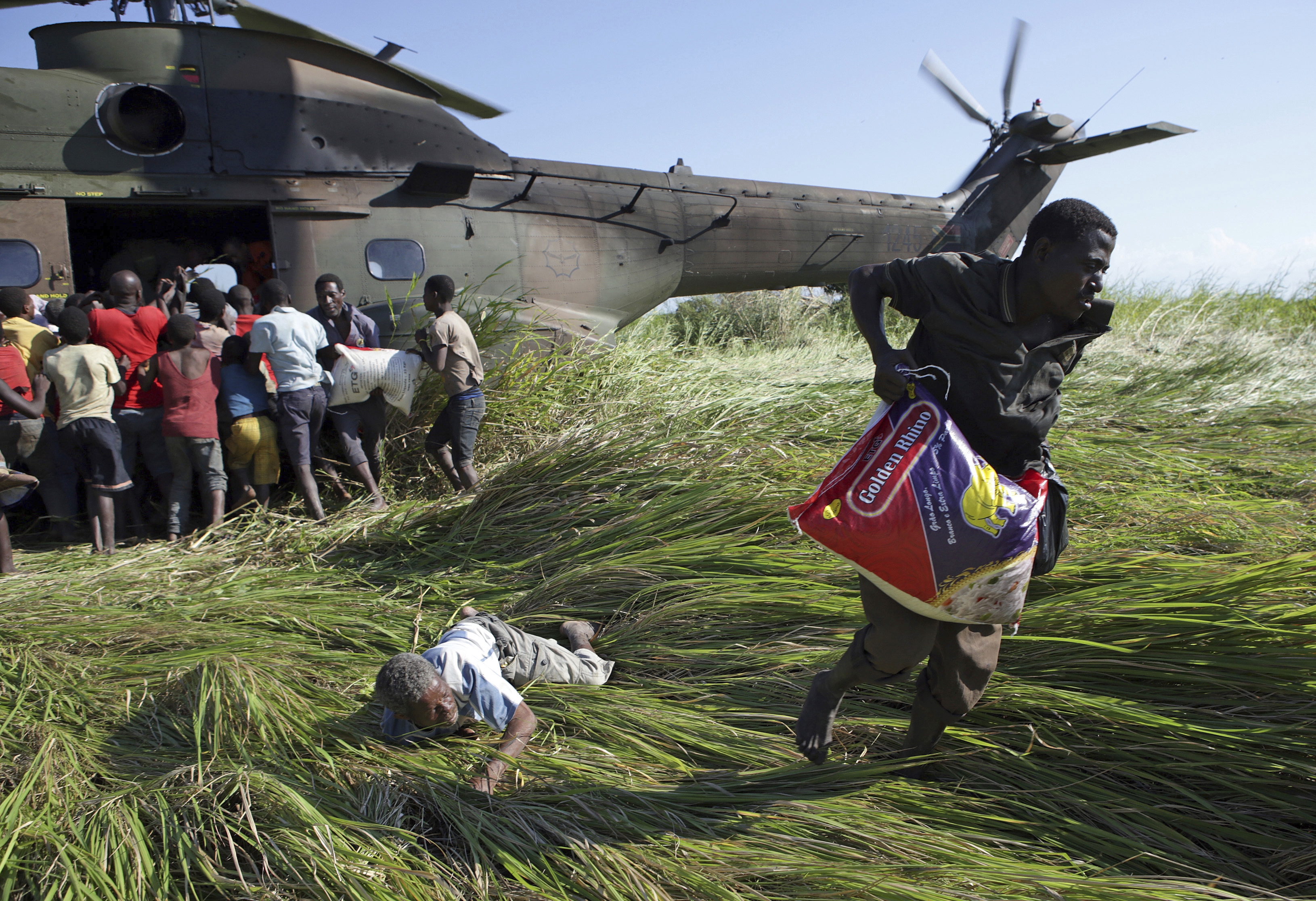 In this photo taken Tuesday, March 26, 2019 an elderly man lies on the ground after his bag of food was snatched from him in a scramble for bags of rice delivered by the South African Airforce helicopter at Nyamatande Village, Mozambique, following the devastating Tropical Cyclone Idai. A second week has begun with efforts to find and help some tens of thousands of people in devastated parts of southern Africa, with some hundreds dead and an unknown number of people still missing. (AP Photo/Phill Magakoe)