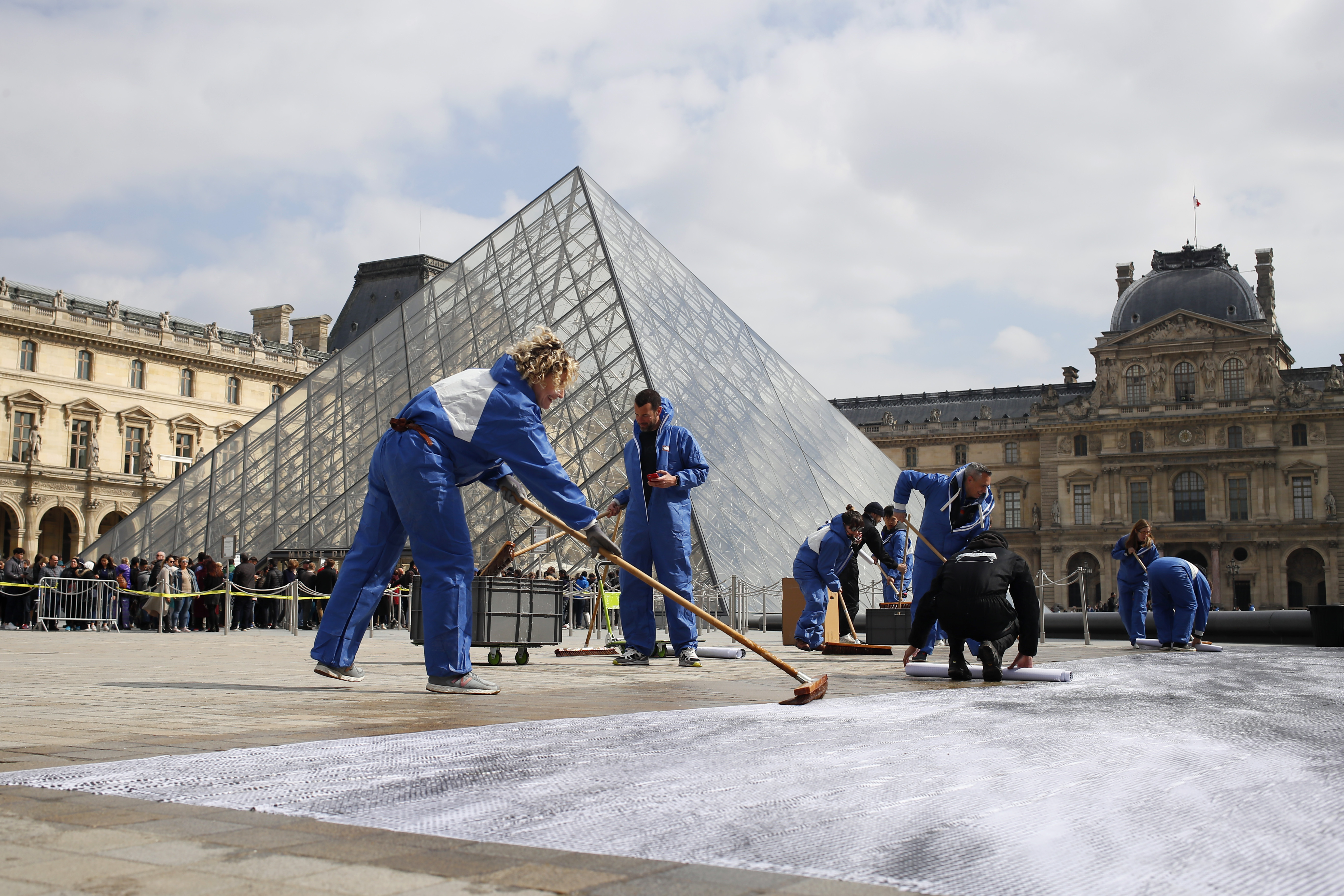 French street artist JR volunteers work in the courtyard of the Louvre Museum near the glass pyramid designed by architect Leoh Ming Pei, in Paris, Wednesday, March 27, 2019 as the Louvre Museum celebrates the 30th anniversary of its glass pyramid. JR project is a giant collage of the pyramid to bring it out of the ground by revealing the foundations of the Napoleon courtyard where it is erected. (AP Photo/Francois Mori)