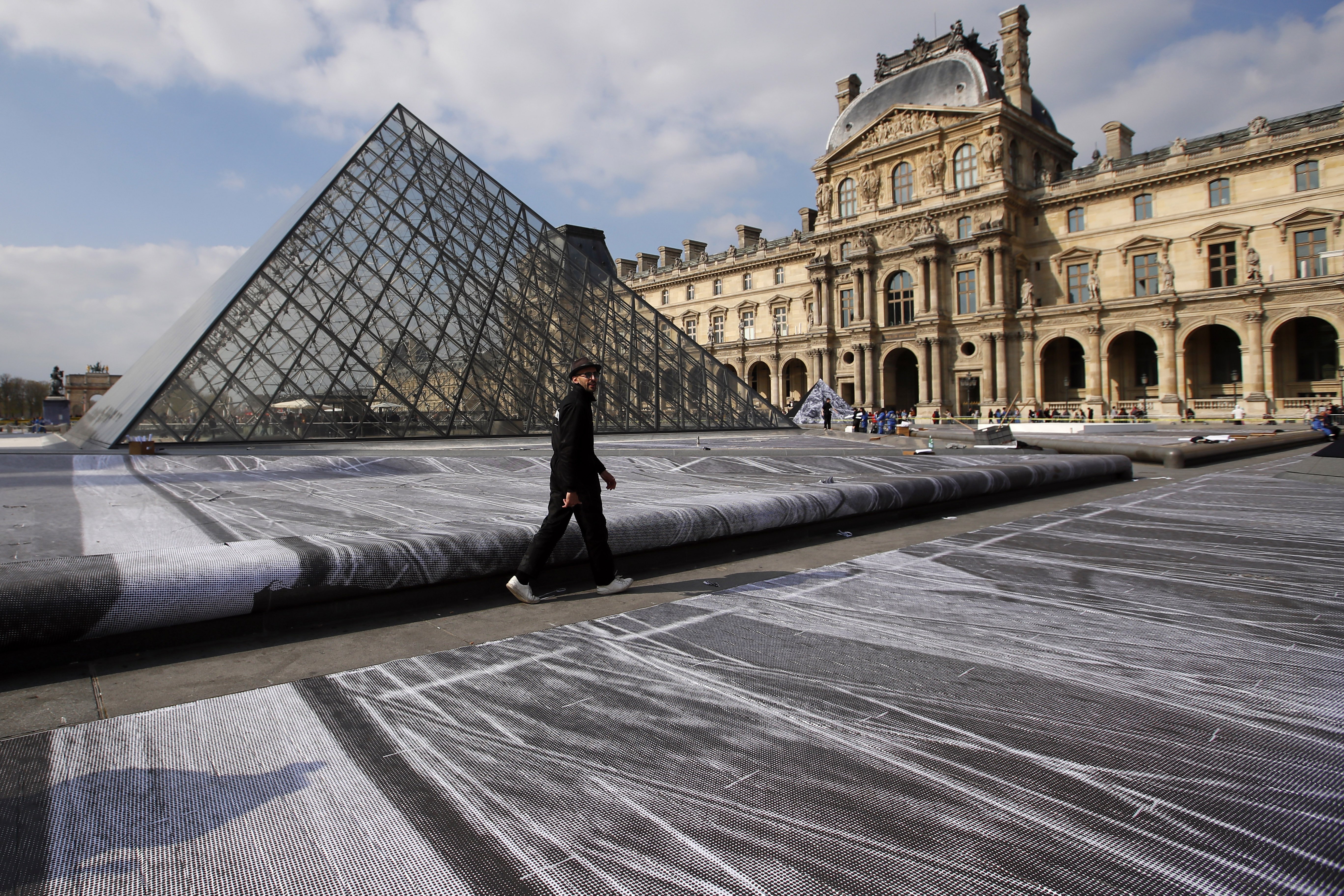 French street artist JR walks in the courtyard of the Louvre Museum near the glass pyramid designed by architect Leoh Ming Pei, in Paris, Wednesday, March 27, 2019 as the Louvre Museum celebrates the 30th anniversary of its glass pyramid. JR project is a giant collage of the pyramid to bring it out of the ground by revealing the foundations of the Napoleon courtyard where it is erected. (AP Photo/Francois Mori)