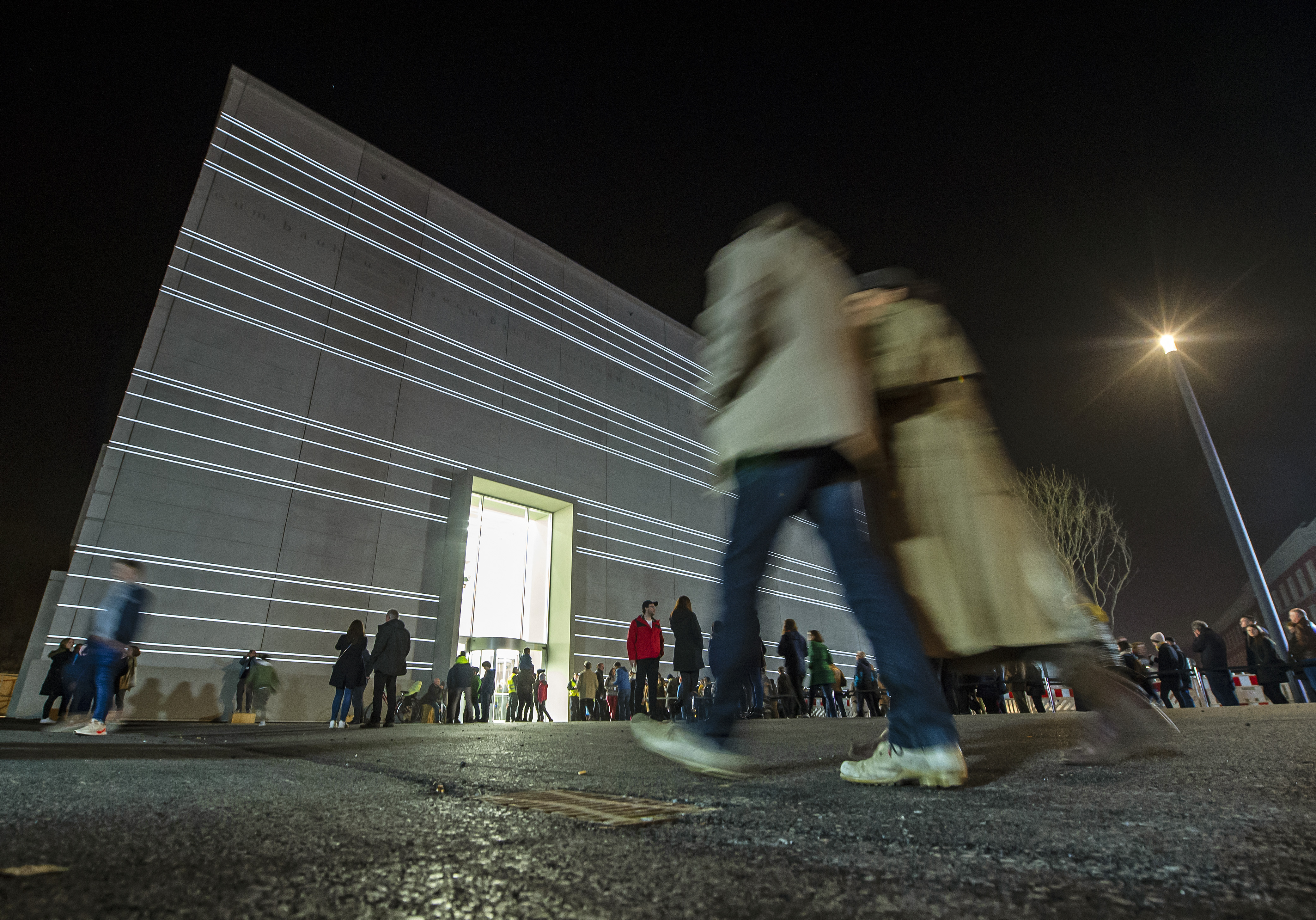 People walk in front of the new Bauhaus Museum building during a light installation performance at the official opening by the Klassik Stiftung Weimar in Weimar, Germany, Friday, April 5, 2019. The museum, designed by Berlin-based Heike Hanada, will focus on the early Bauhaus that was founded in Weimar in 1919 and stayed there until 1925. (AP Photo/Jens Meyer)