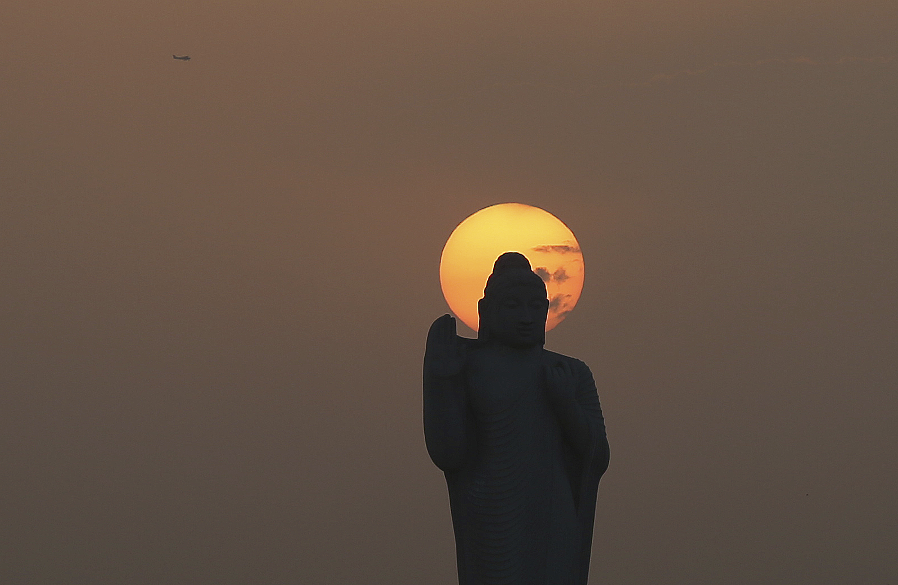 A statue of Buddha is silhouetted against the setting sun as an aircraft flies above the Lake Hussain Sagar on Bhuddha Purnima festival in Hyderabad, India, Saturday, May 18, 2019. The festival marks the birth, enlightenment and death of Buddha.(AP Photo/Mahesh Kumar A.)
